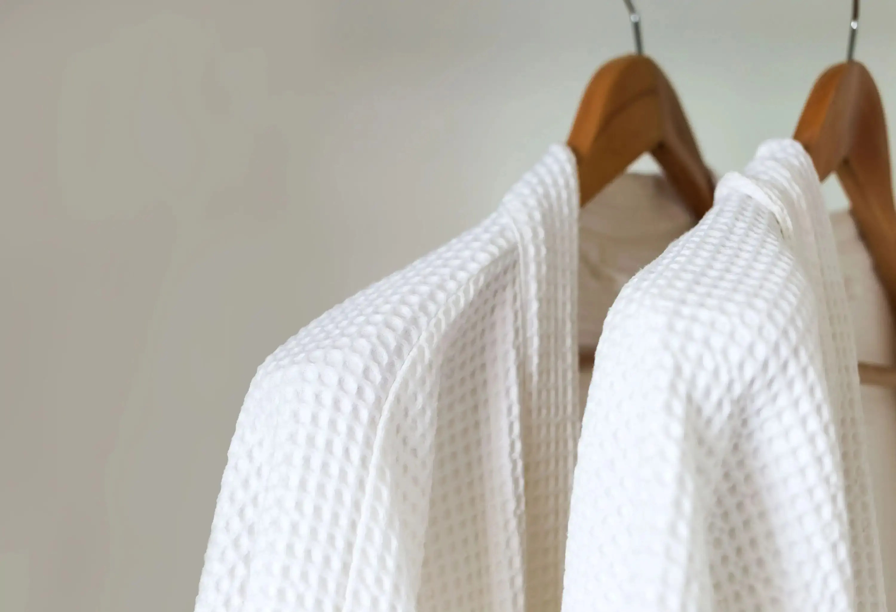 Two clean white robes hanging on wooden hangers.