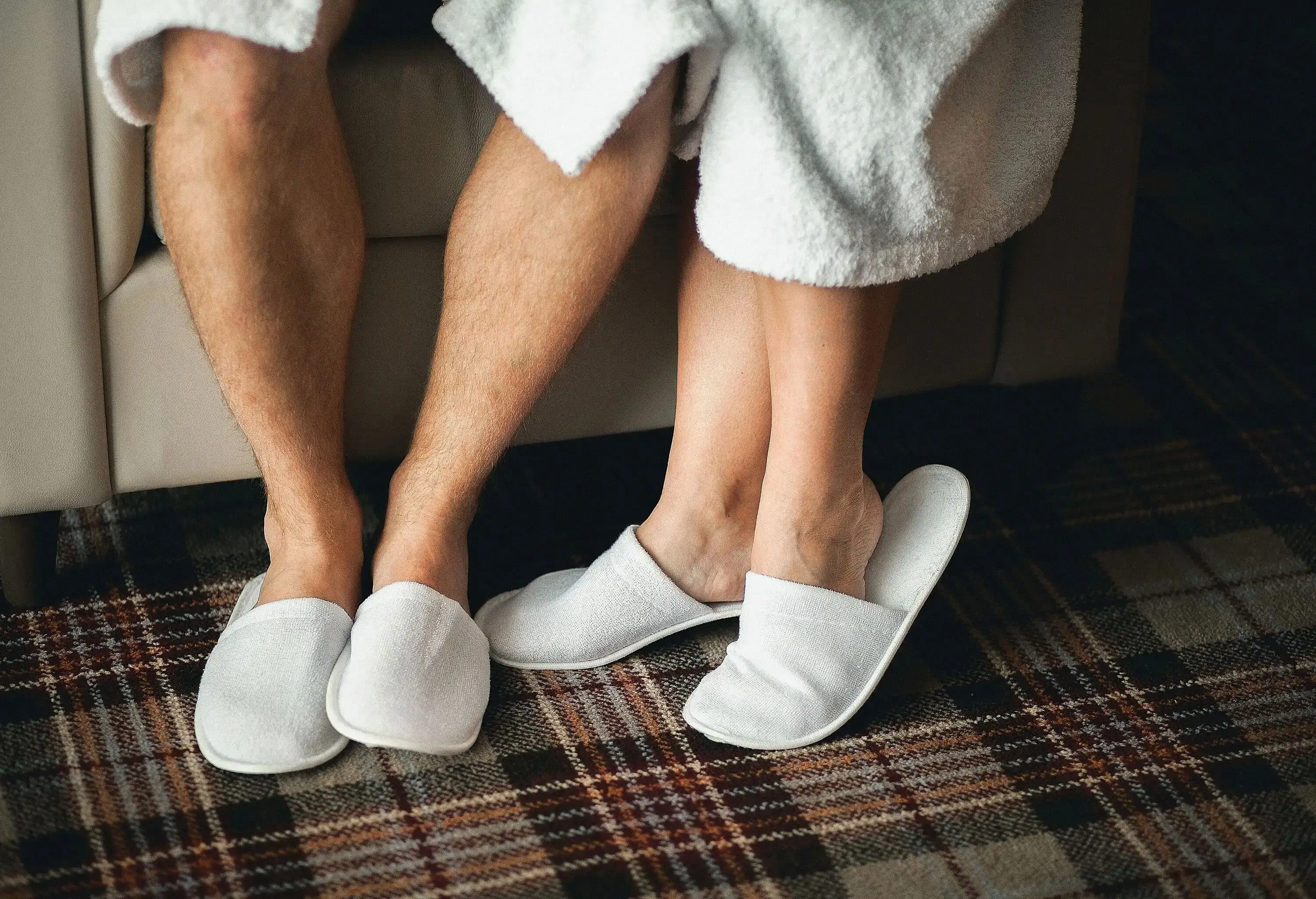 Two pairs of feet wearing white slippers.