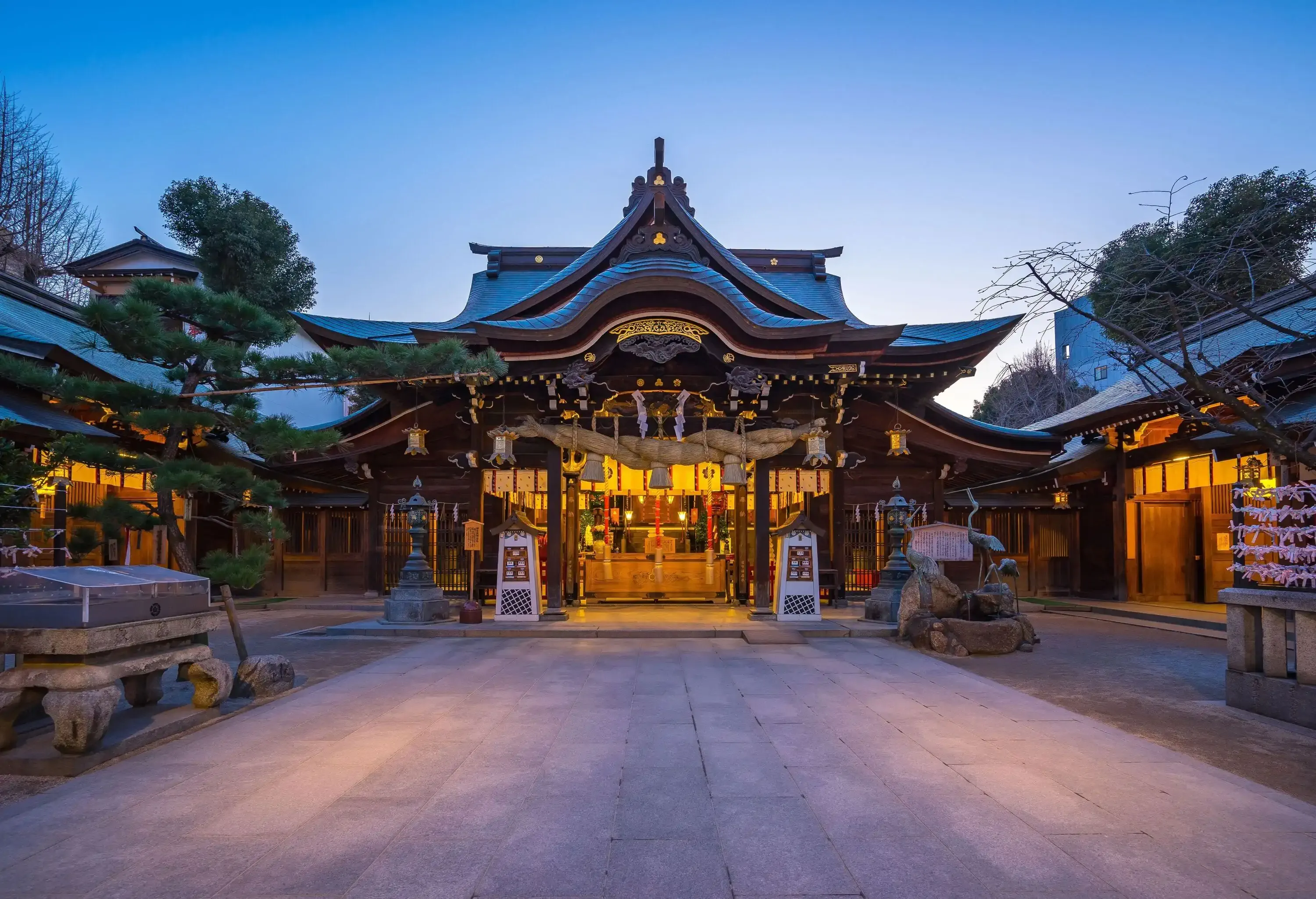 A night-time view of an empty path towards a Japanese shrine with illuminated interiors.