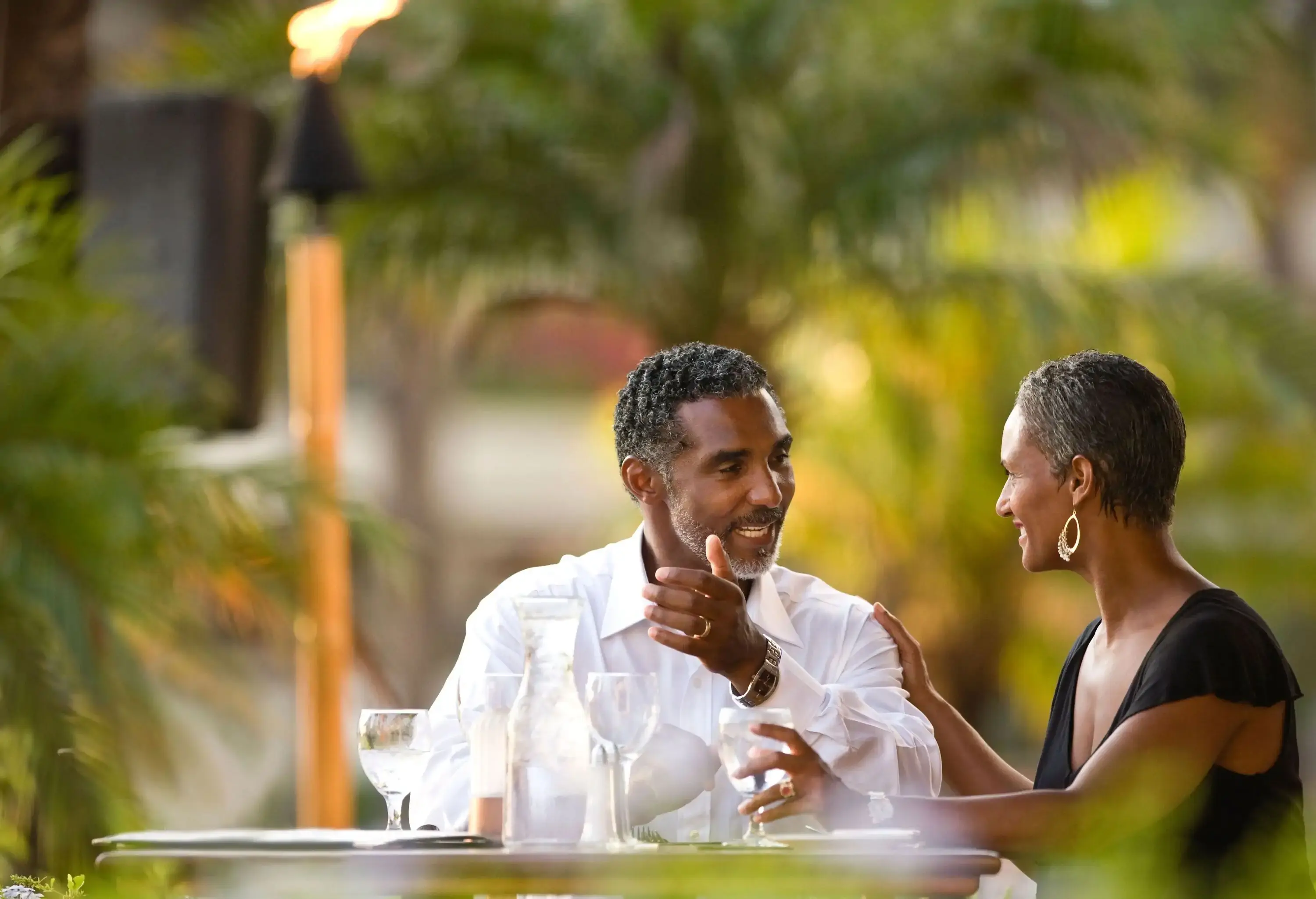 A couple shares a romantic date at an outdoor restaurant, with a lush green background providing a natural and serene ambiance for their special moment.