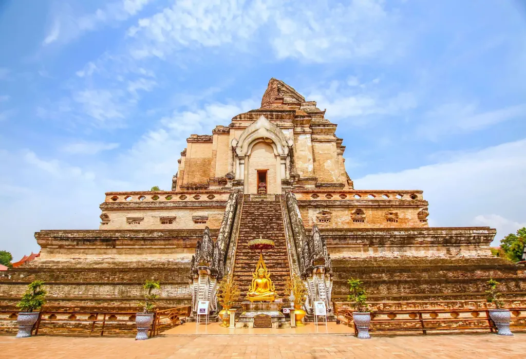 A Buddhist temple with an imposing stupa and a golden statue at the base of the staircase flanked by serpent heads.
