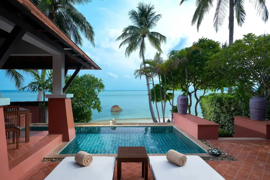 Luxurious tropical beachfront setting featuring a private pool, surrounded by lush palm trees. 