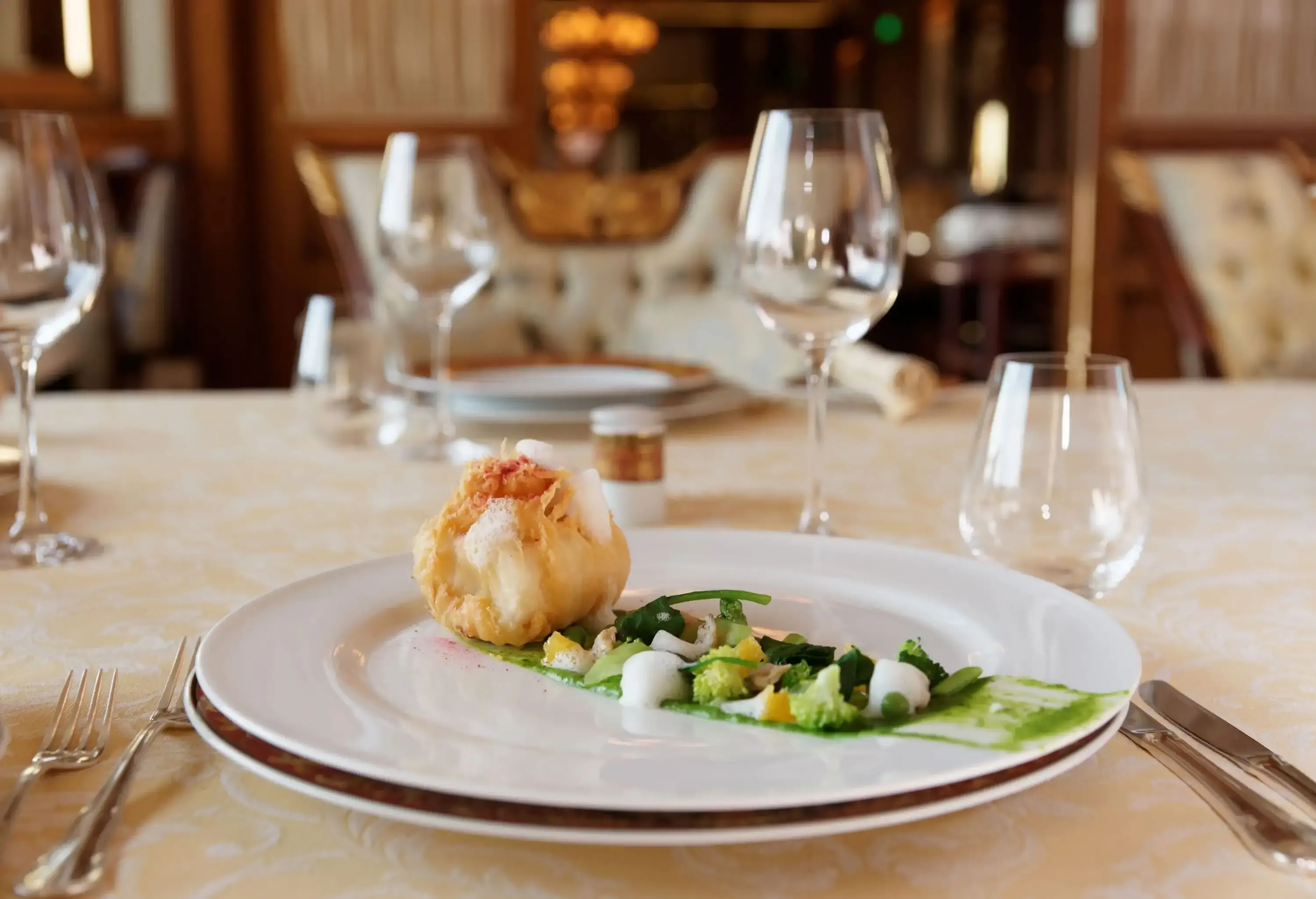 A well-plated gourmet meal and empty wine glasses on a restaurant table.