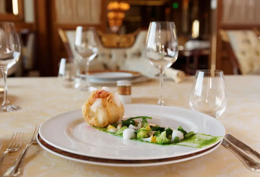 A well-plated gourmet meal and empty wine glasses on a restaurant table.