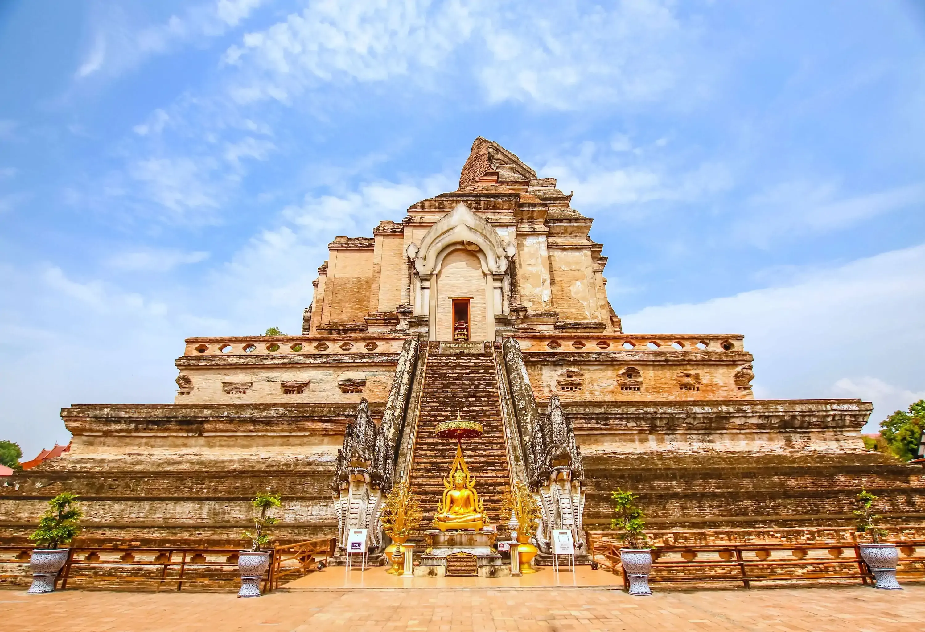 A Buddhist temple with an imposing stupa and a golden statue at the base of the staircase flanked by serpent heads.