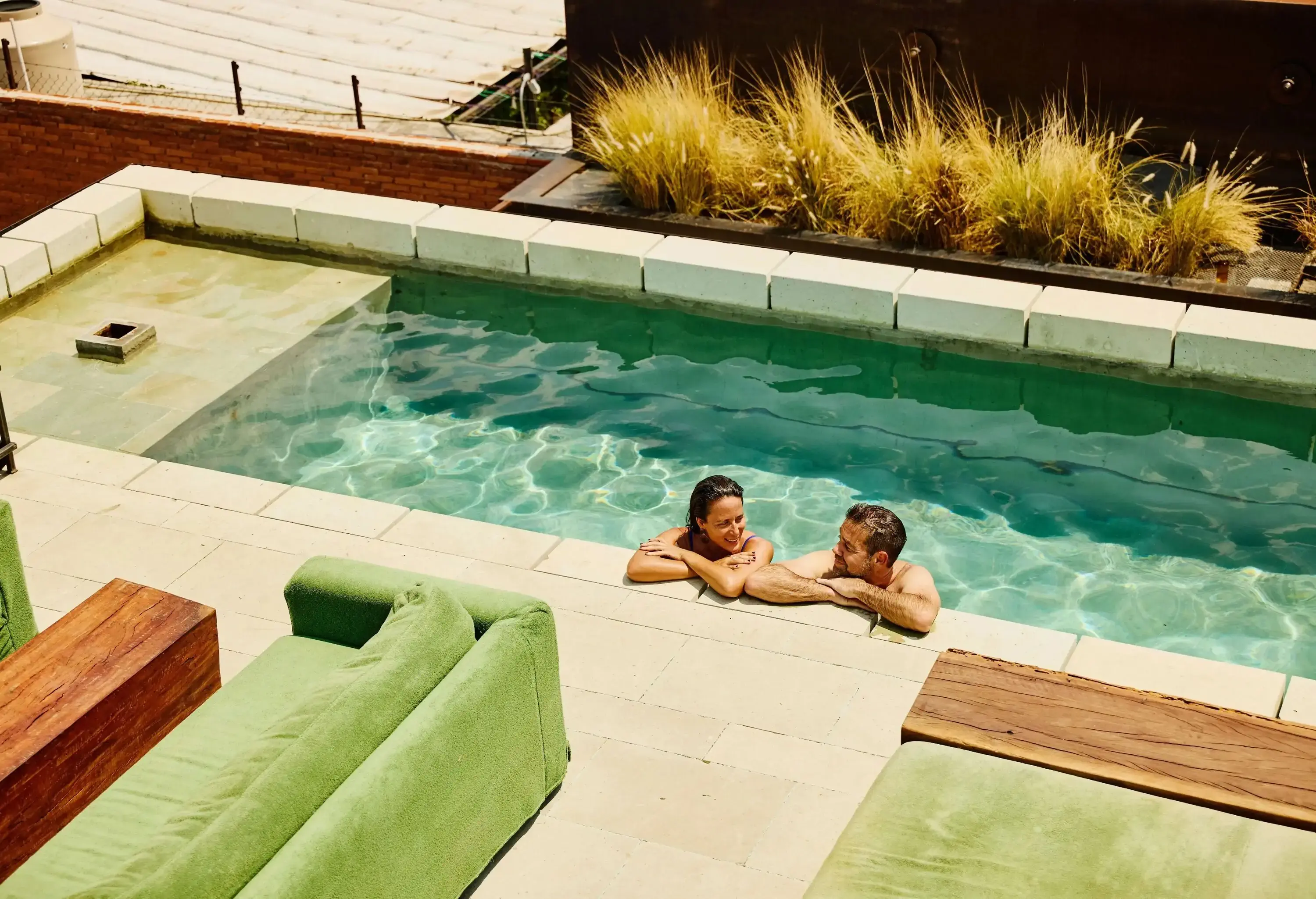 Wide high angle view of smiling mature couple relaxing at edge of luxury hotel rooftop pool during vacation to Mexico