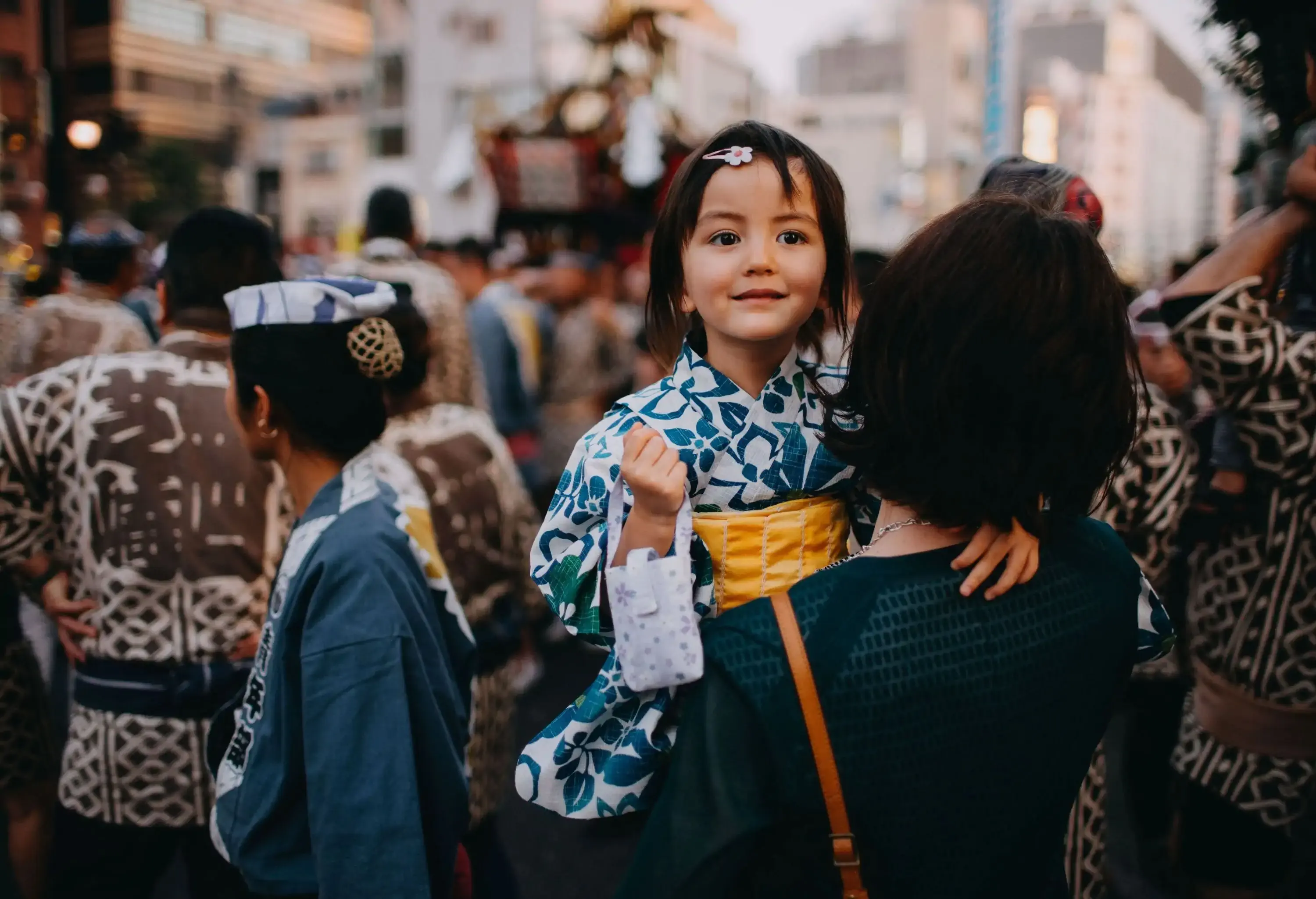 A girl in a kimono carried by her mother in a crowded area.