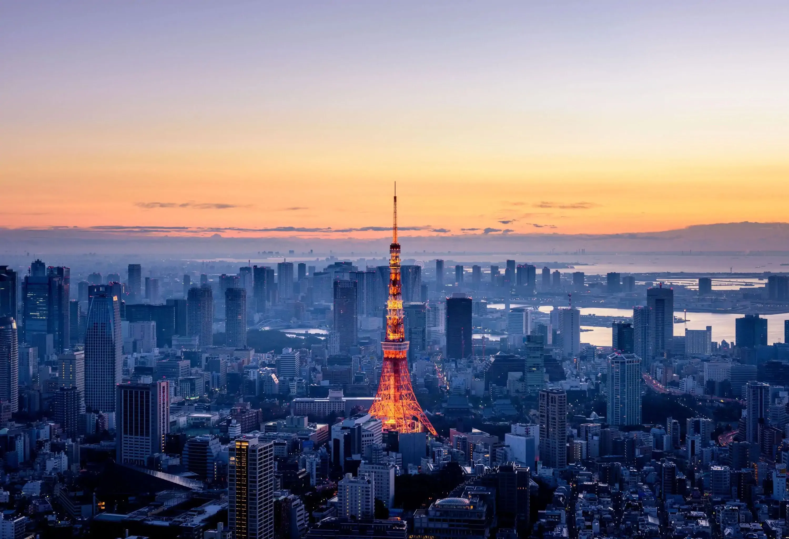 An illuminated central tower surrounded by numerous tall buildings dominates a sprawling city at dawn.
