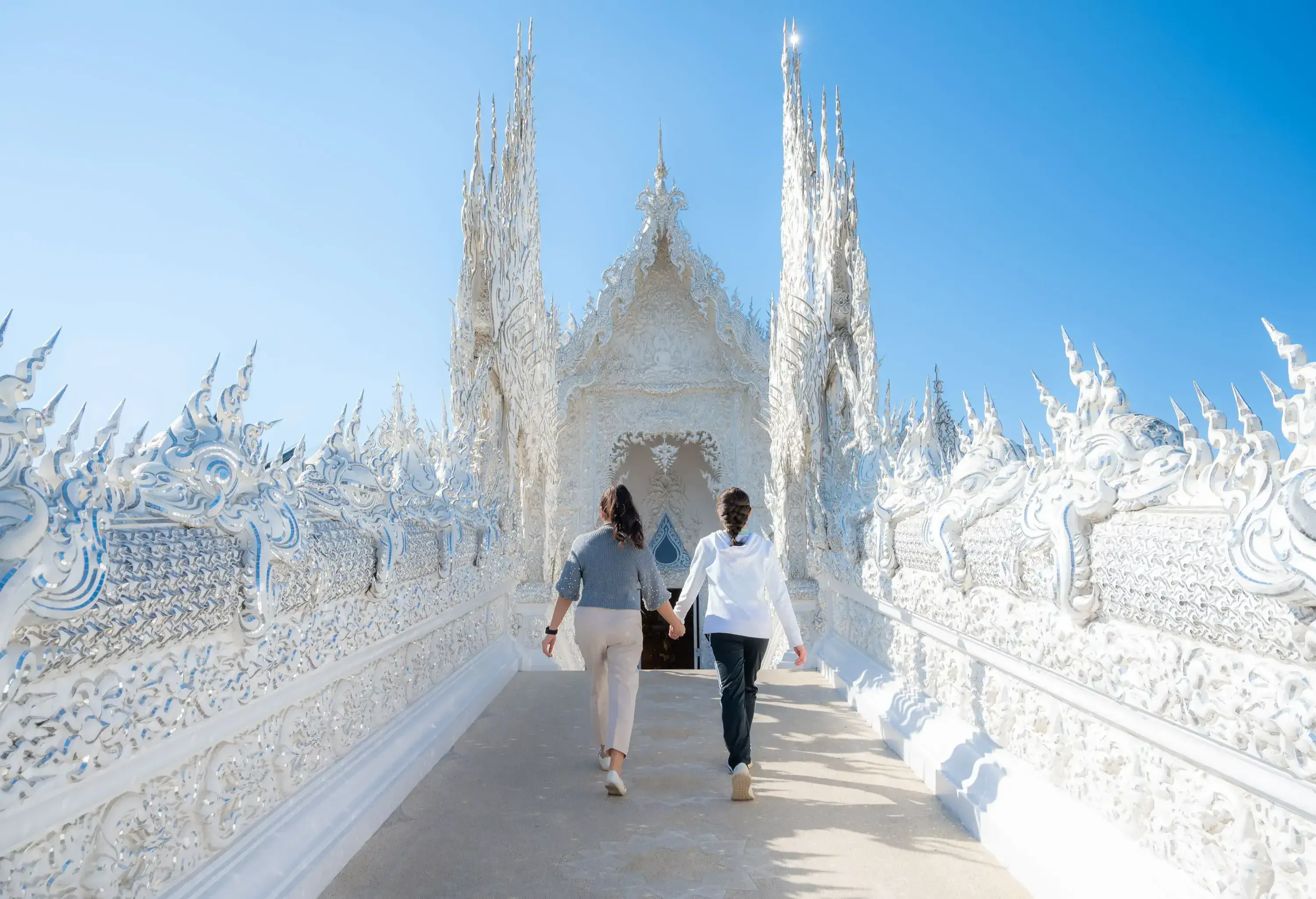 Two women strolling hand in hand on a walkway at the Wat Rong Khun.
