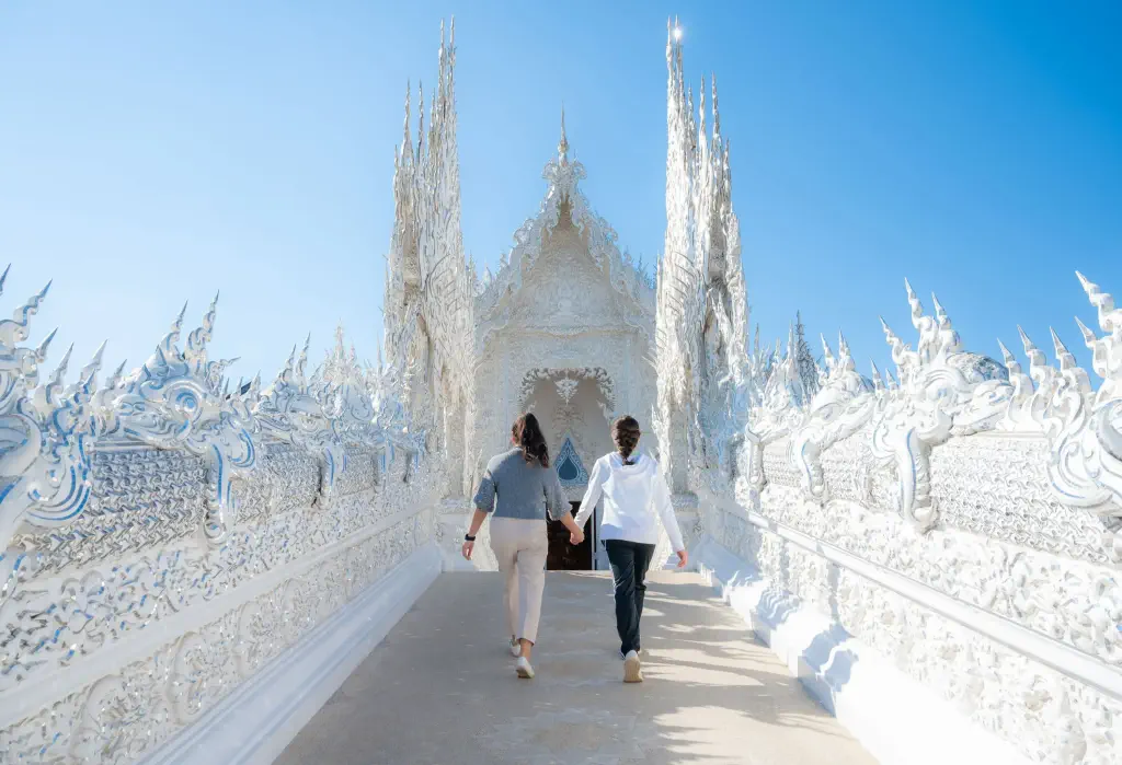 Two women strolling hand in hand on a walkway at the Wat Rong Khun.