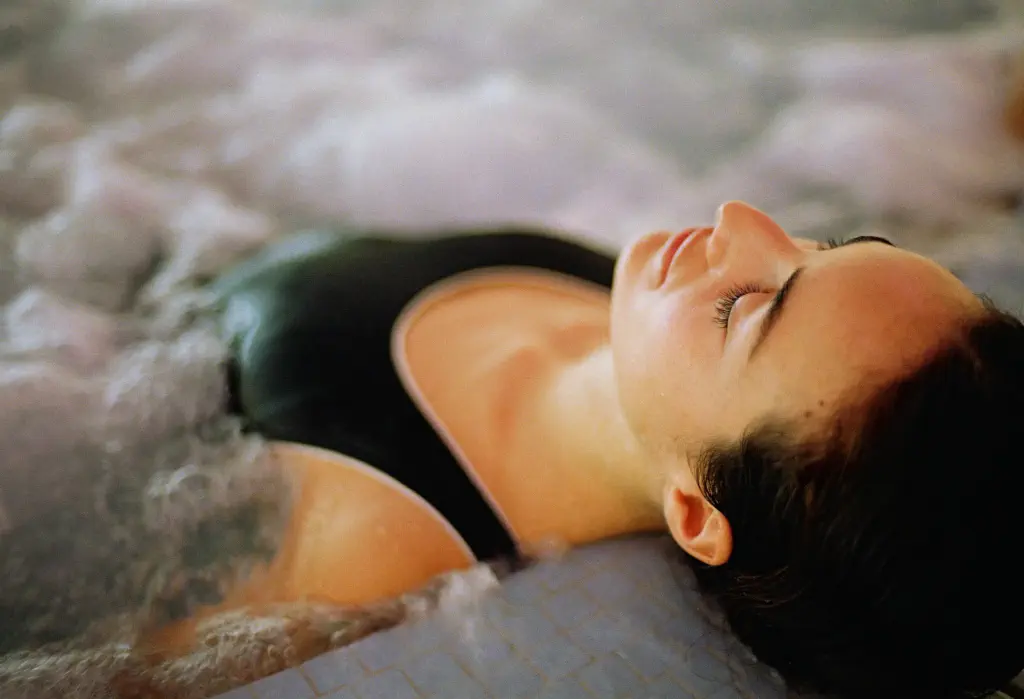 A woman in a black swimsuit relaxes in a hot tub with her eyes closed.