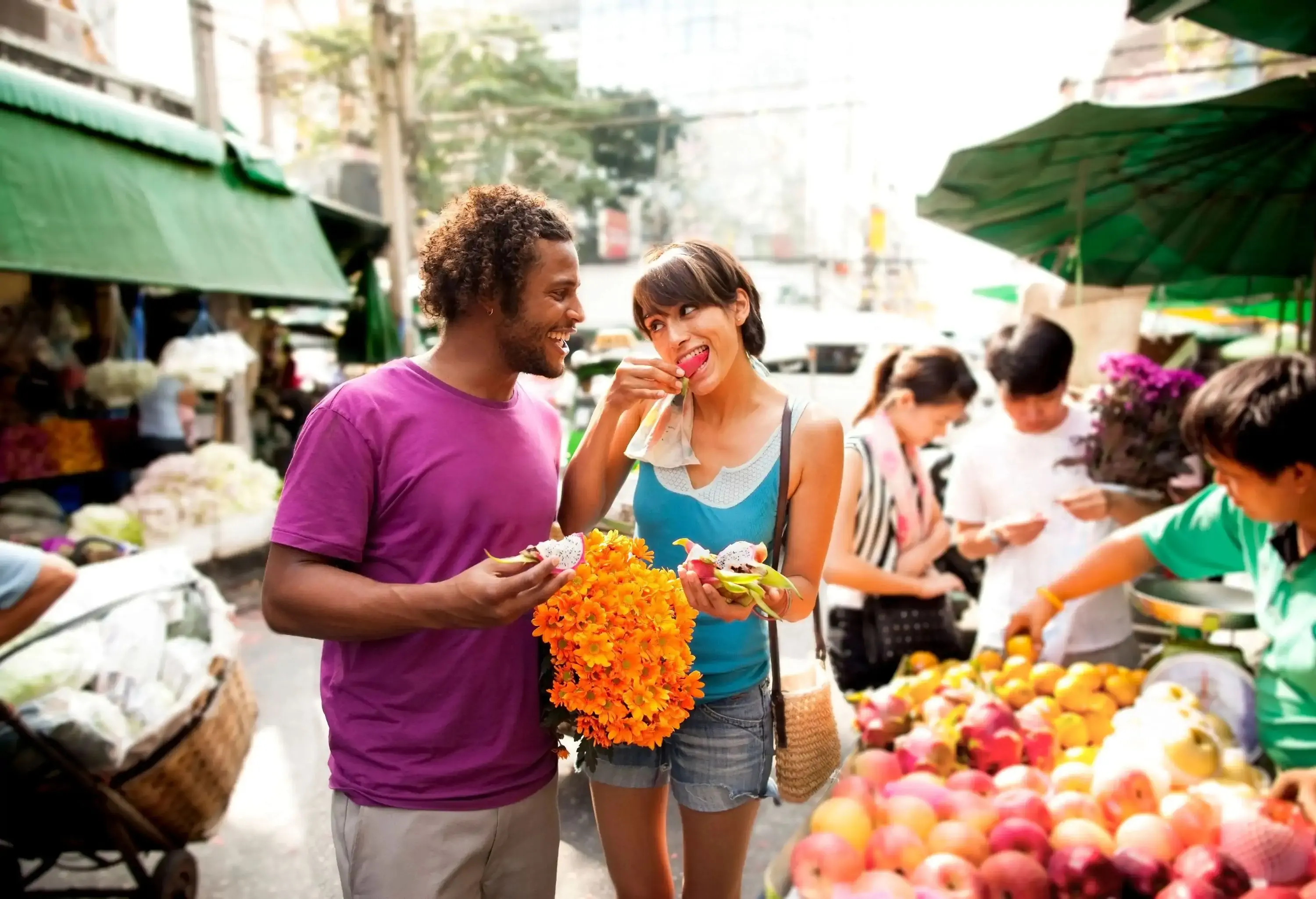 Two happy people eating a dragon fruit in the centre of a market.