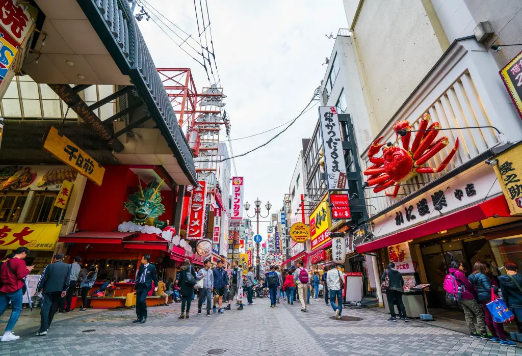 A crowded street lined with restaurants and shops with colourful advertisement billboards.