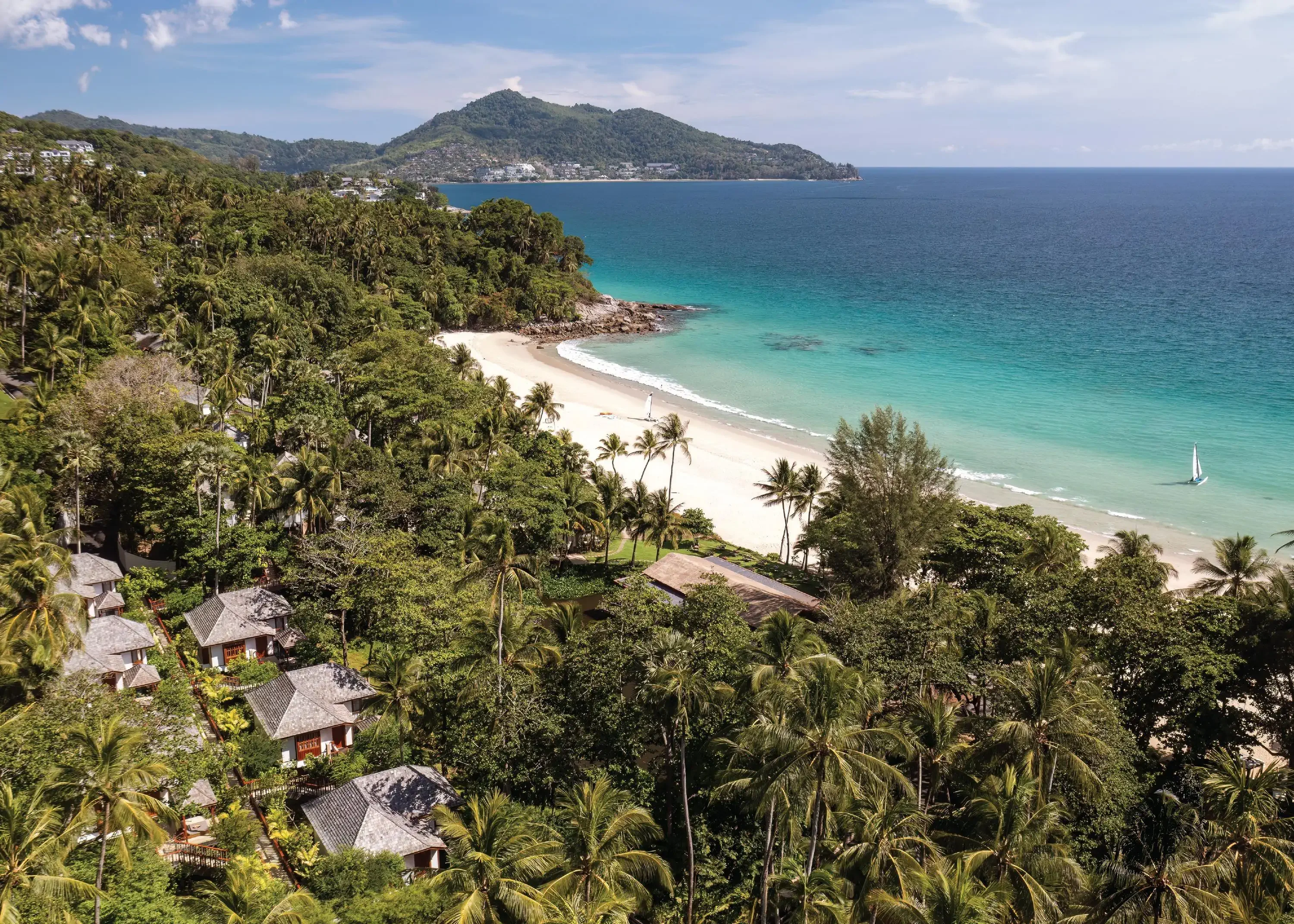 Aerial view of hotel villas in a tropical forest by a white sandy beach