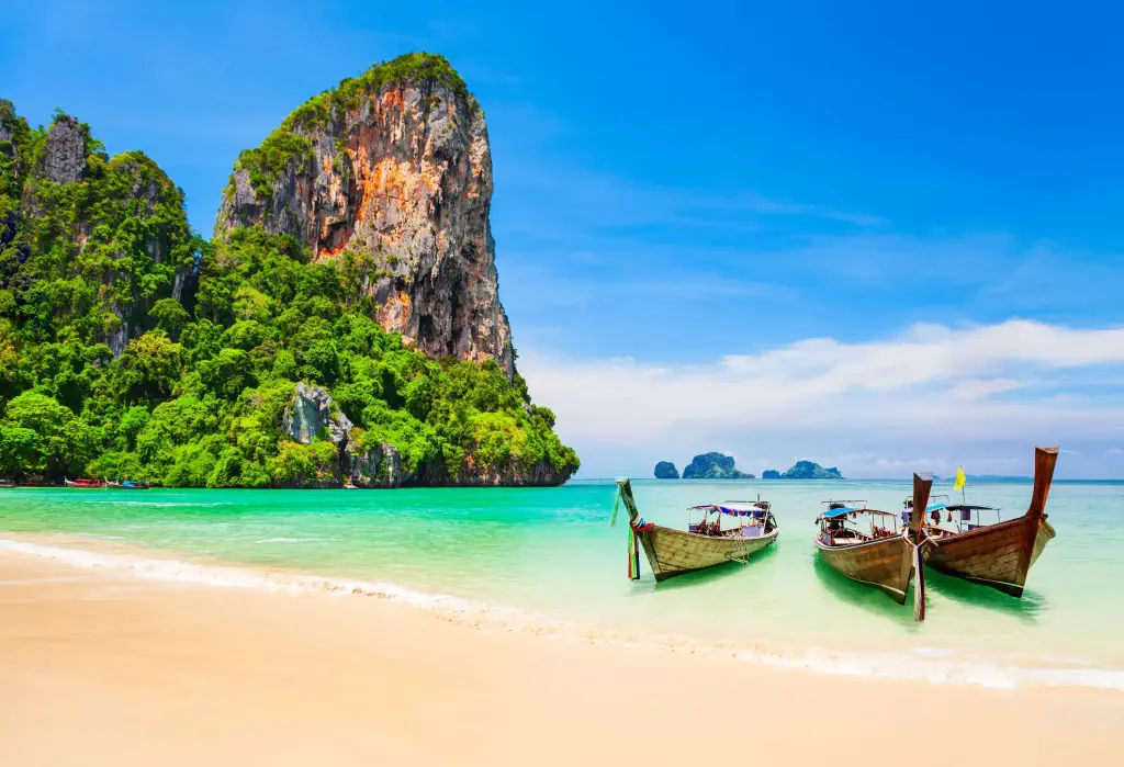 Three long-tail boats on the beach with steep-sided mountains in the backdrop.