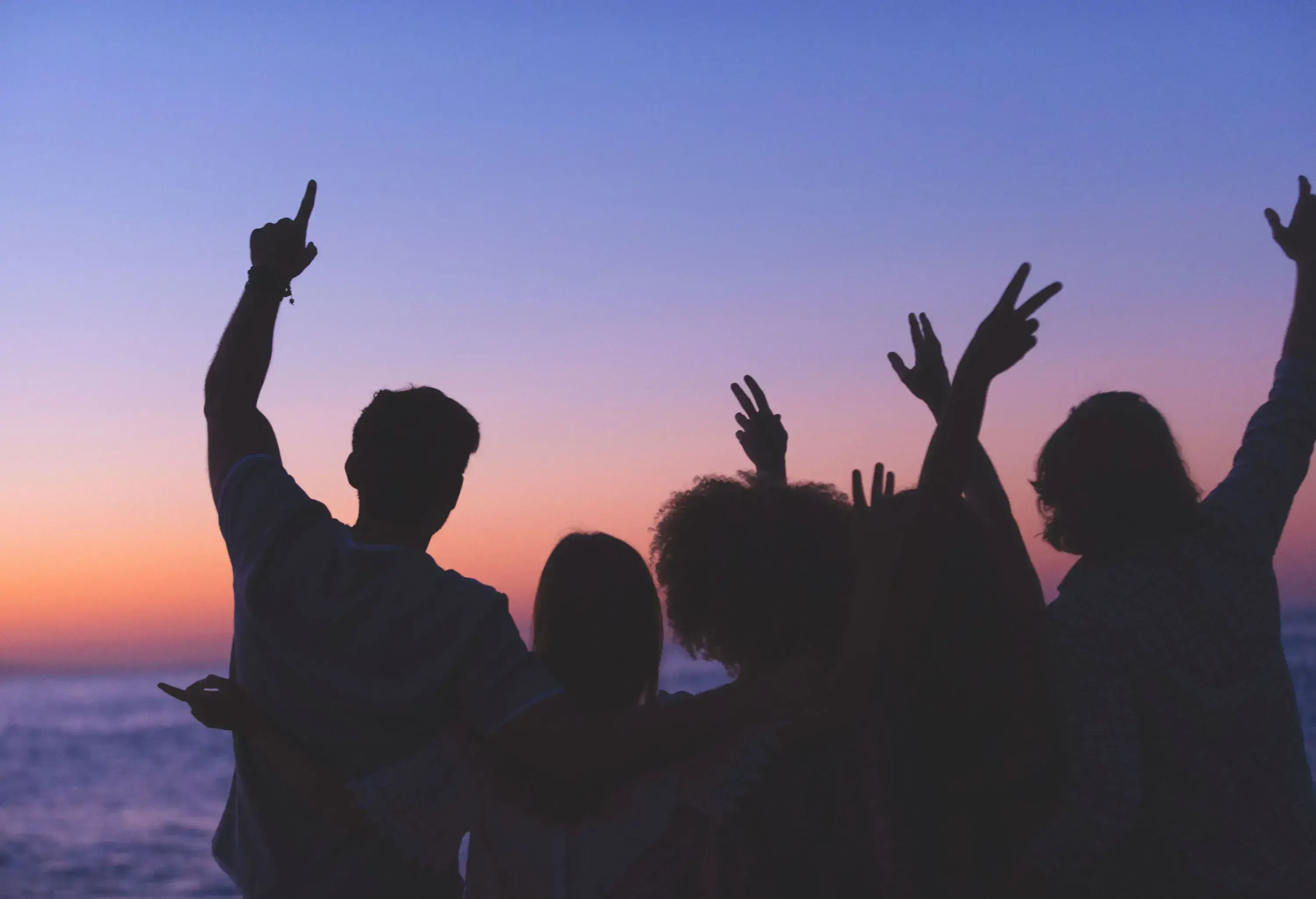 A silhouette of a group with their arms around each other looking across the sea.