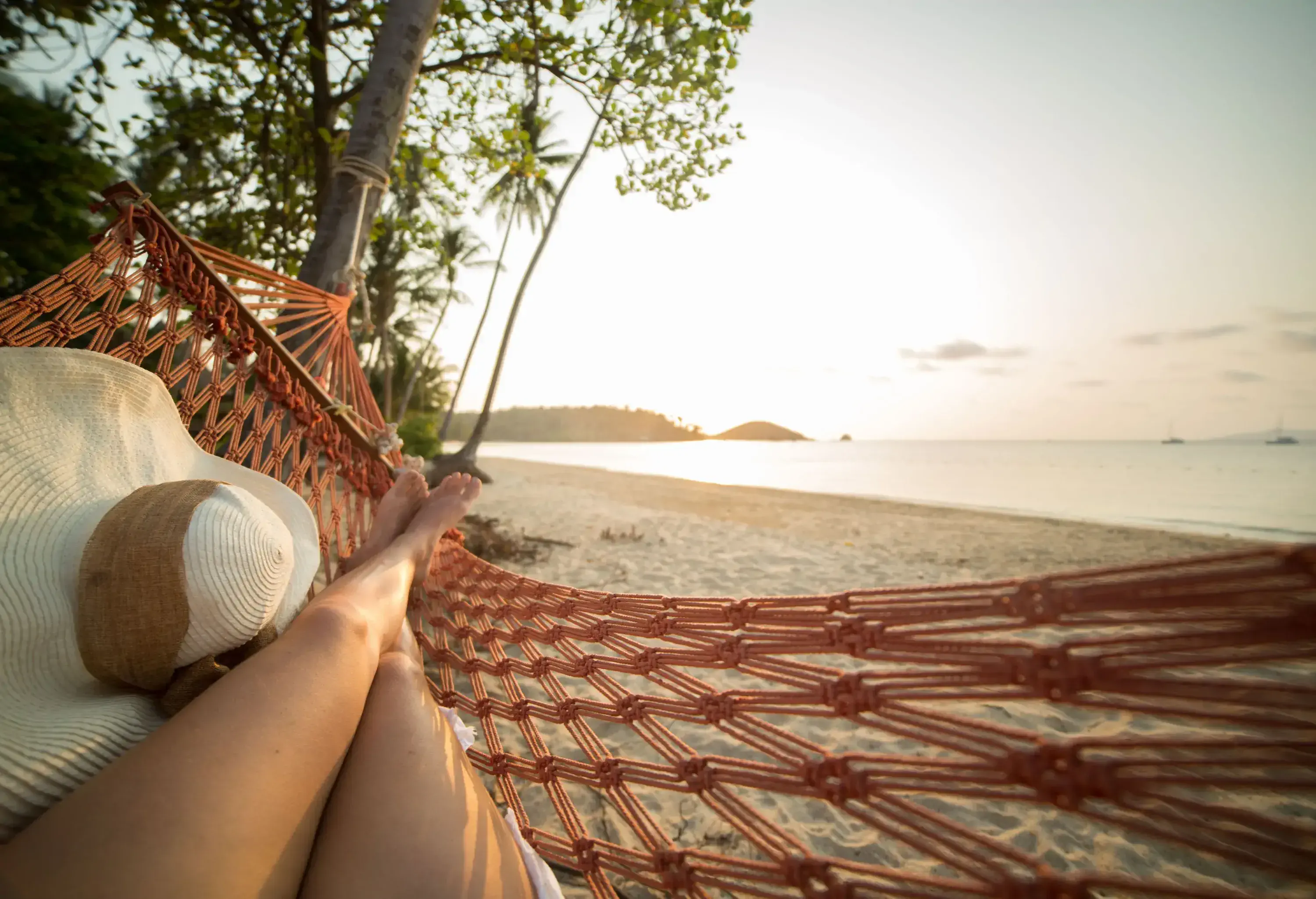 A woman lying on a hammock on the beach with views of the ocean.