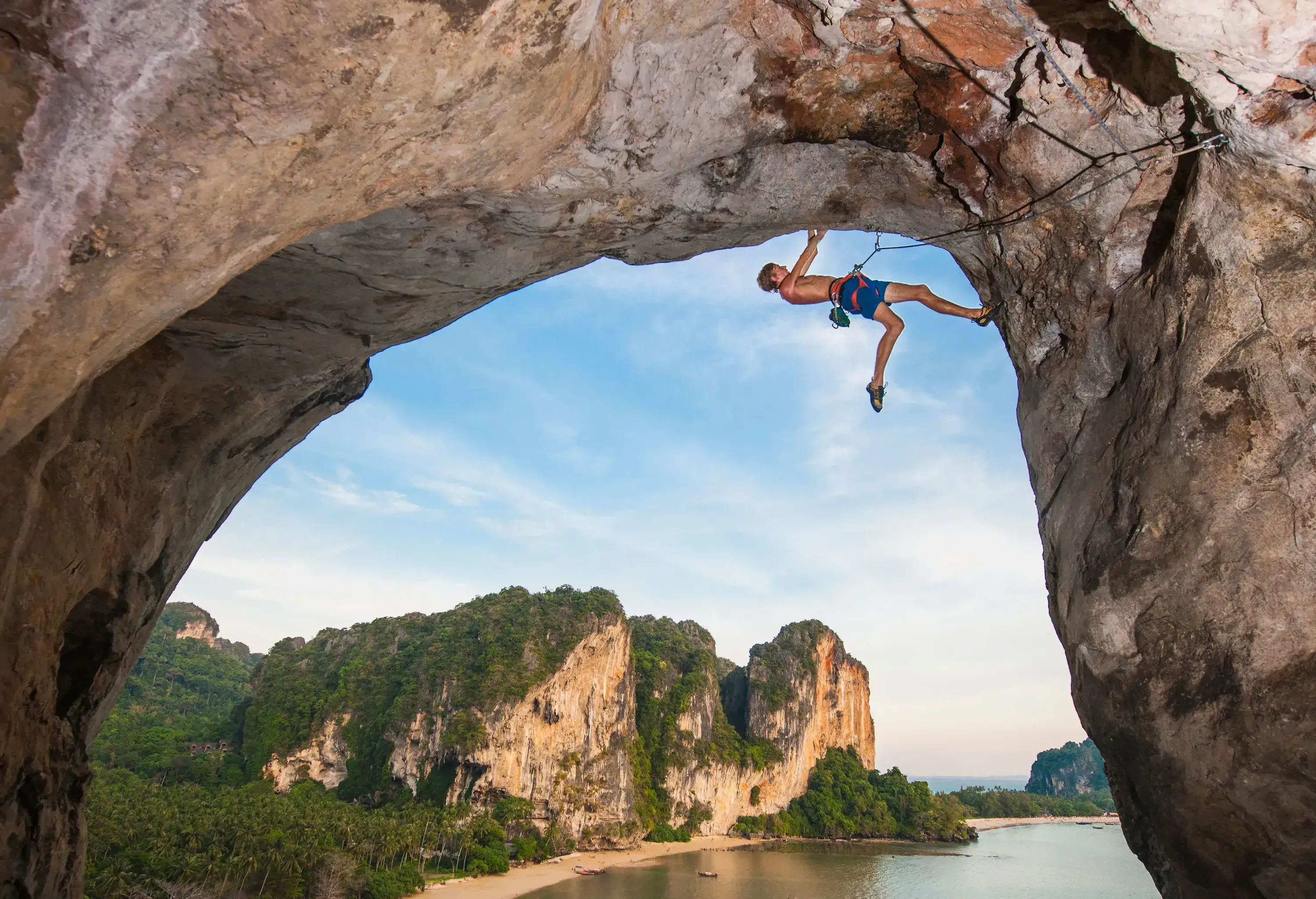 An active male climbing the underside of a natural arch in the sea.