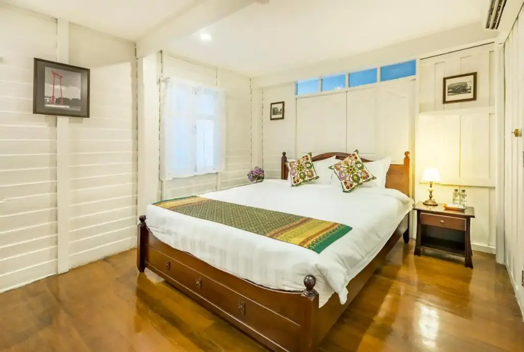 Inviting bedroom with white walls, wooden floors, and a large wooden bed adorned with decorative pillows and a colorful runner.