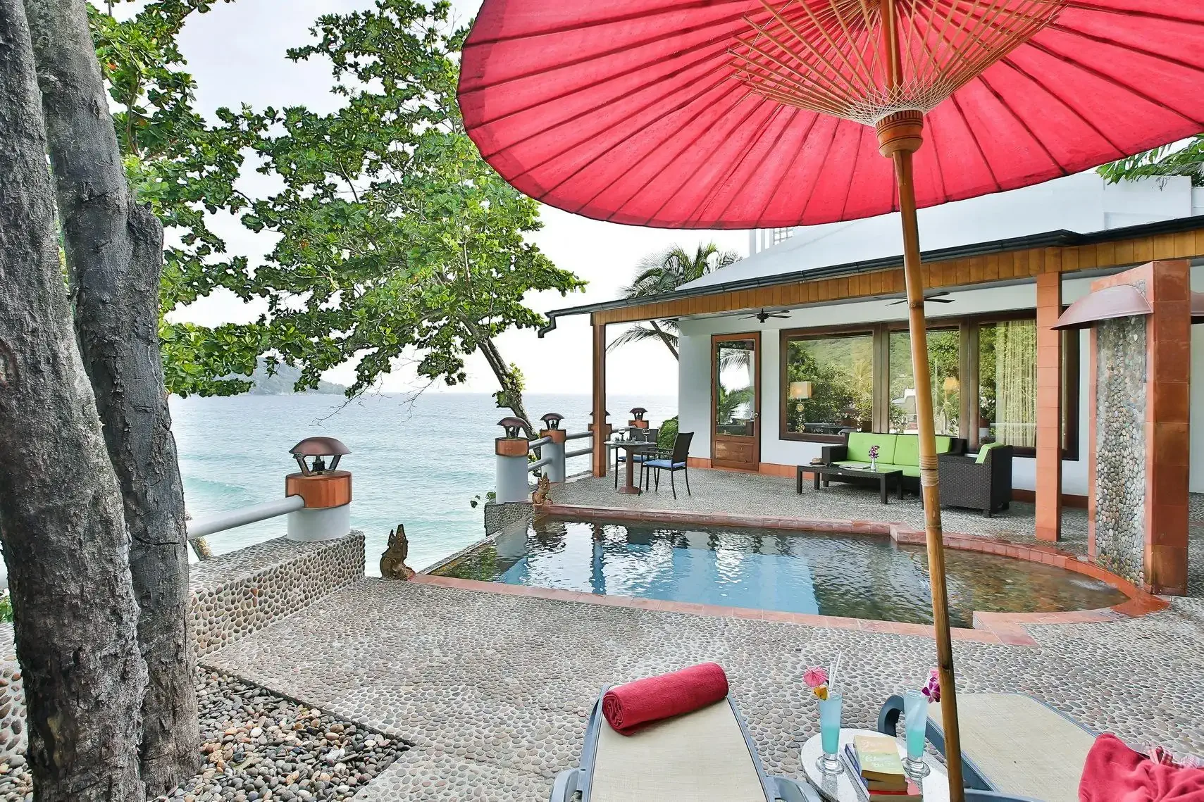 A plunge pool of a hotel by the sea with a red parasol