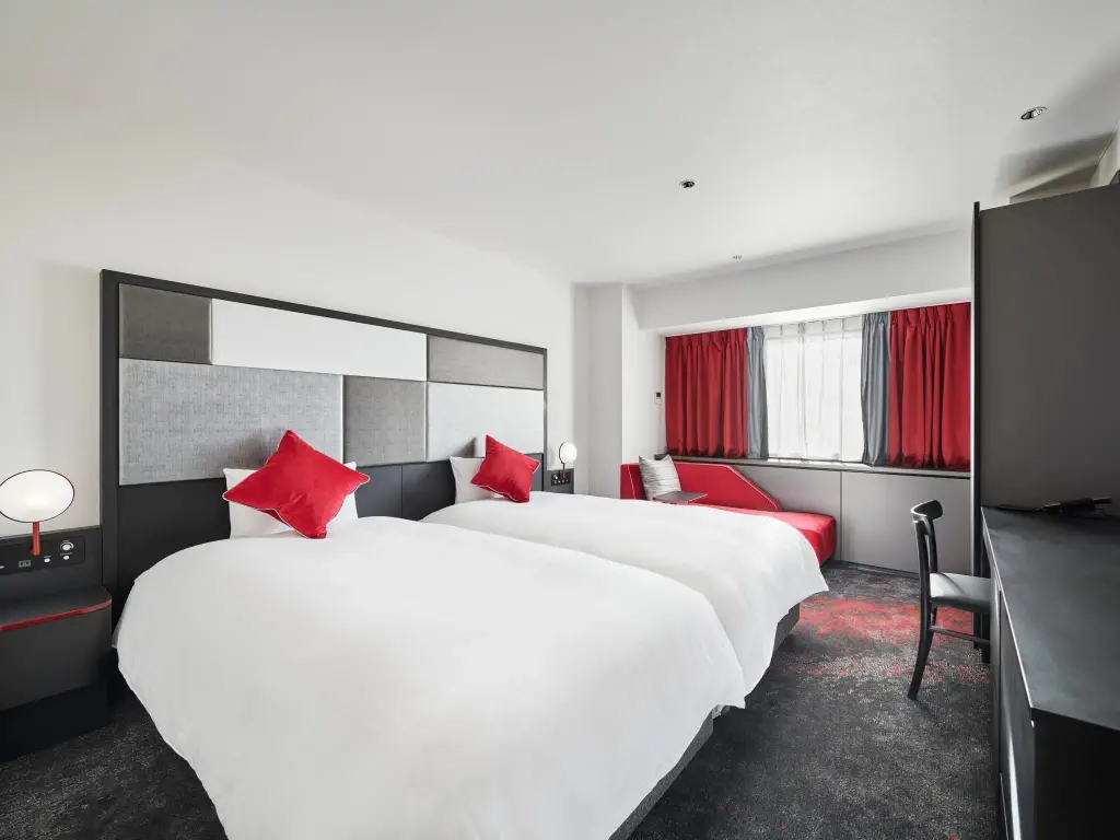 Minimalist hotel bedroom with two double beds and red accents
