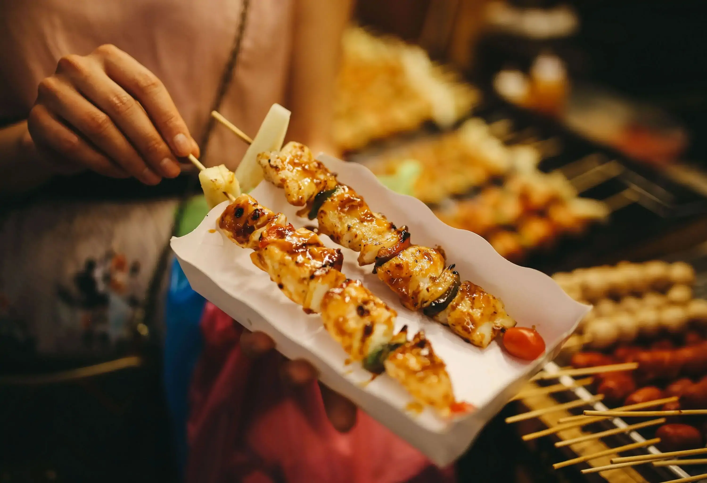 Two chicken skewers with vegetables on a stick placed on a white paper tray.