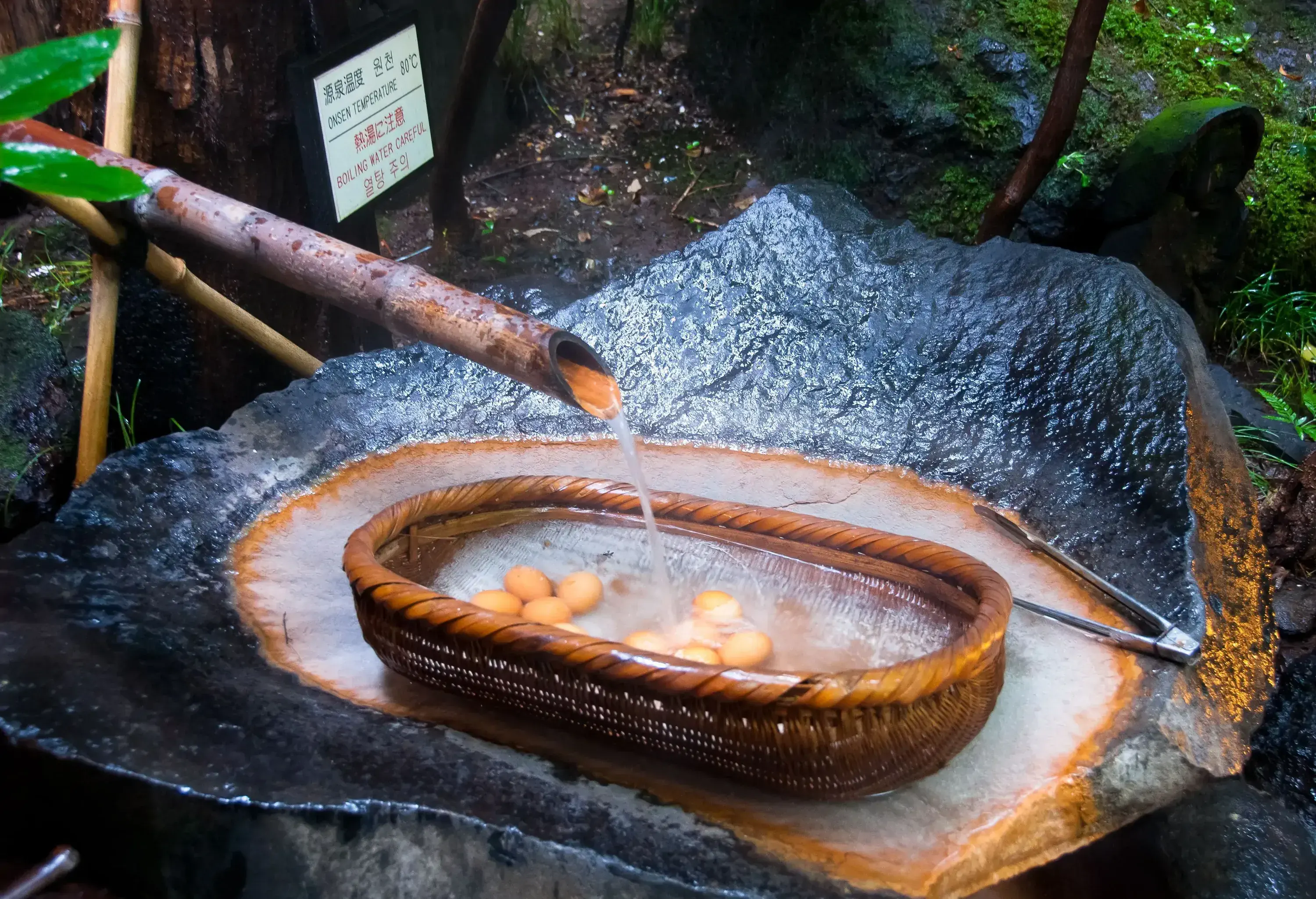 Brown eggs on a wicker basket being cooked in thermal boiling water carved in a stone.