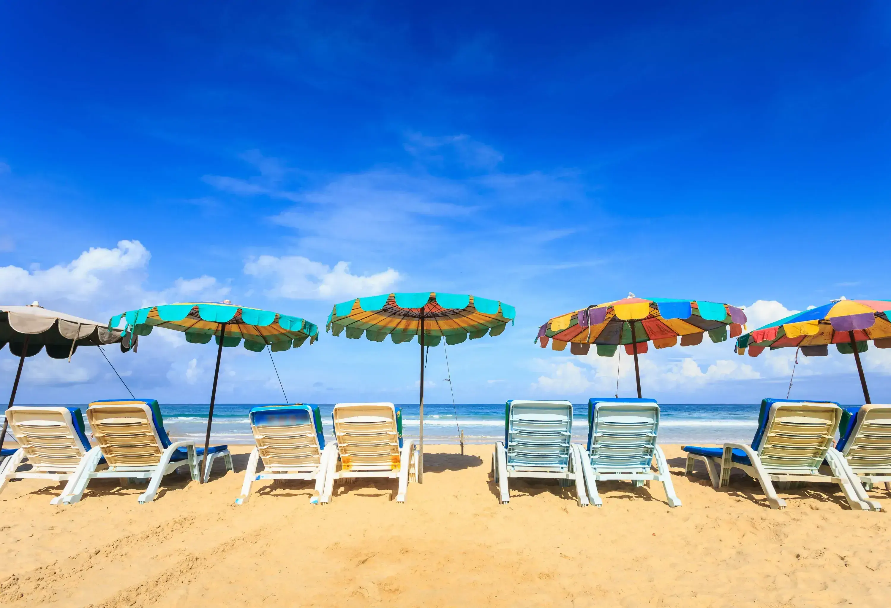 Sunloungers under colourful umbrellas line the golden sand beach.