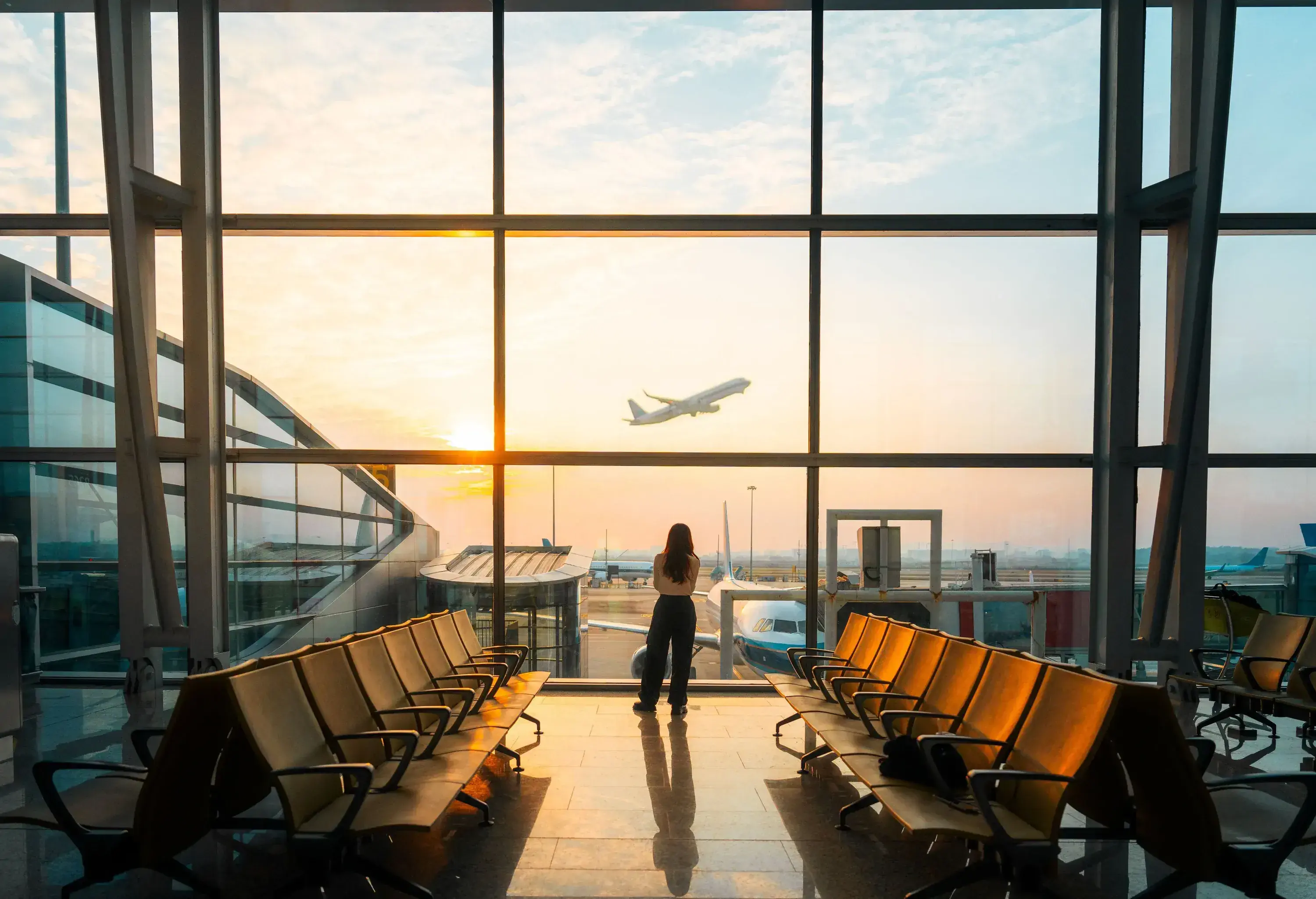 Woman using a smartphone at sunset looking out to a landing strip inside an airport