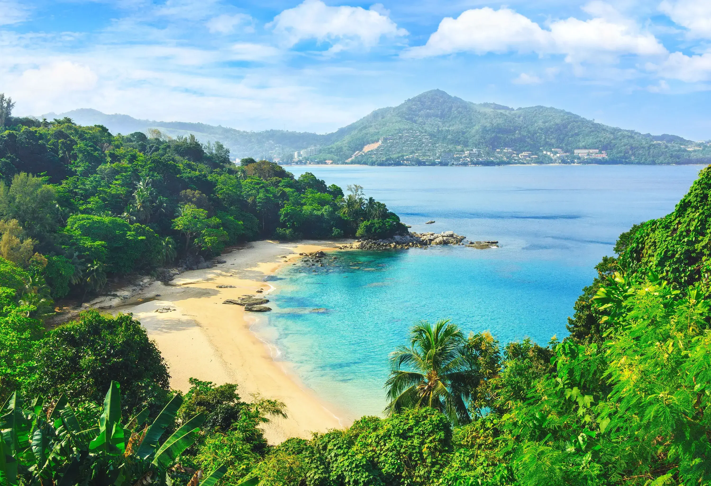 A remote beach along hills covered in lush vegetation with vast bay views.