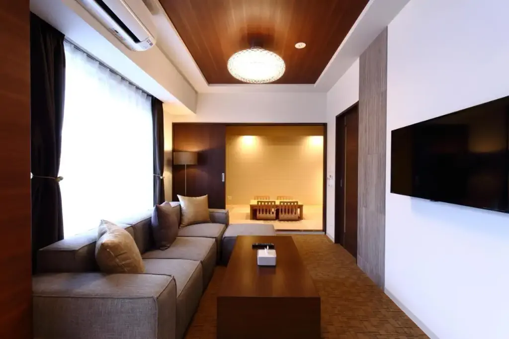 Hotel lounge with grey sofa in front of tv with door over a dining room in japanese style