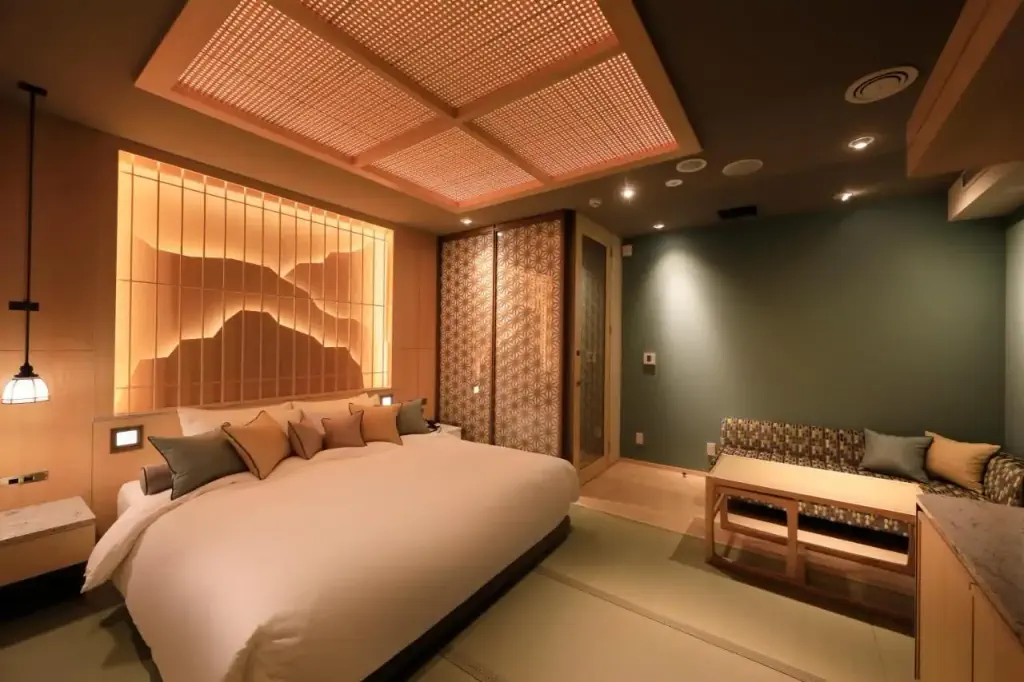 Warm, cozy bedroom with a large bed adorned with pillows. Soft overhead lighting and wooden wall decor create a serene, elegant atmosphere.