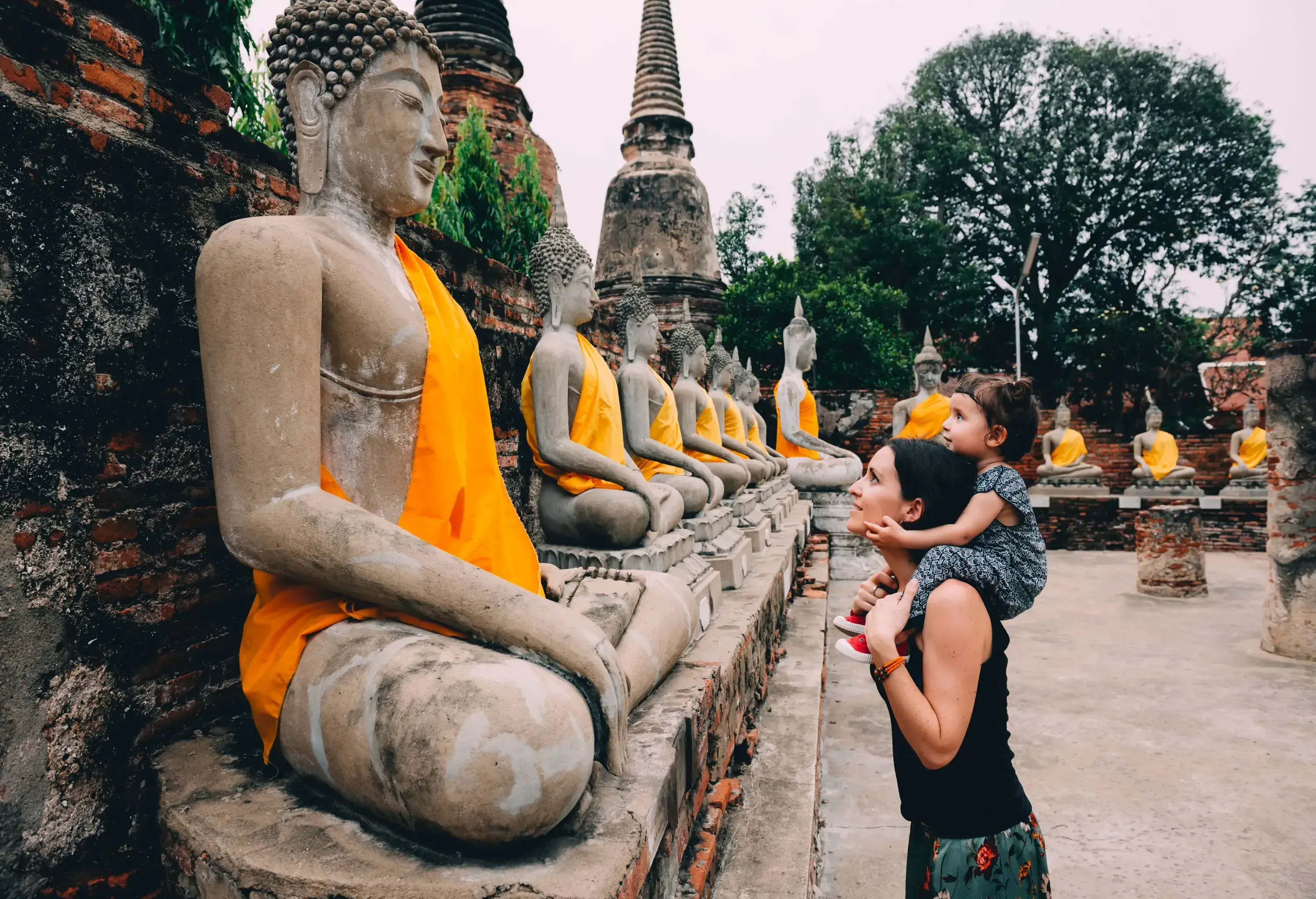 A mother carrying her daughter in her shoulder, looking at the rows of Buddha statues.