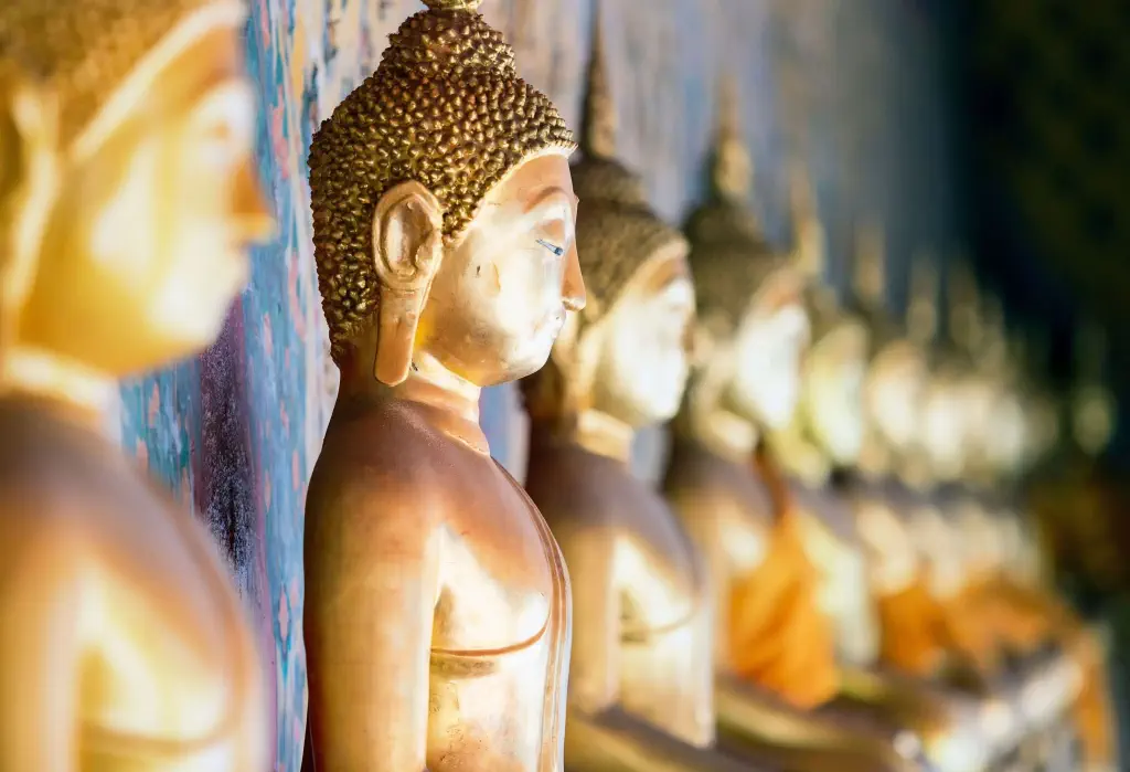 A line of golden Buddha statues sitting with their backs on the wall.