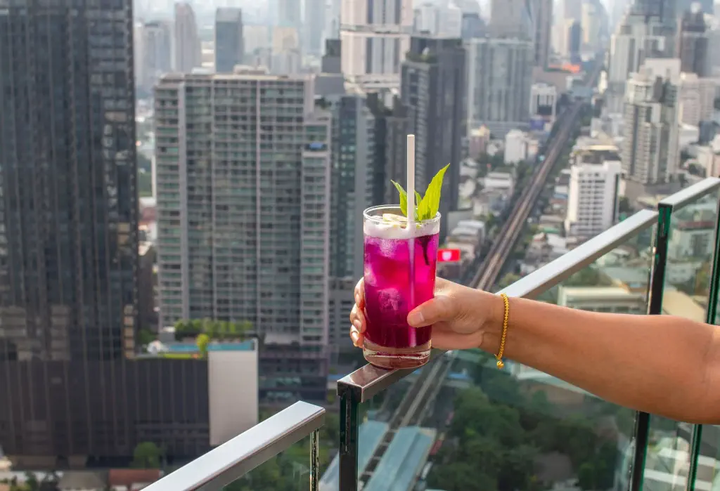 A hand holding a cocktail over the glass barrier of a rooftop bar.