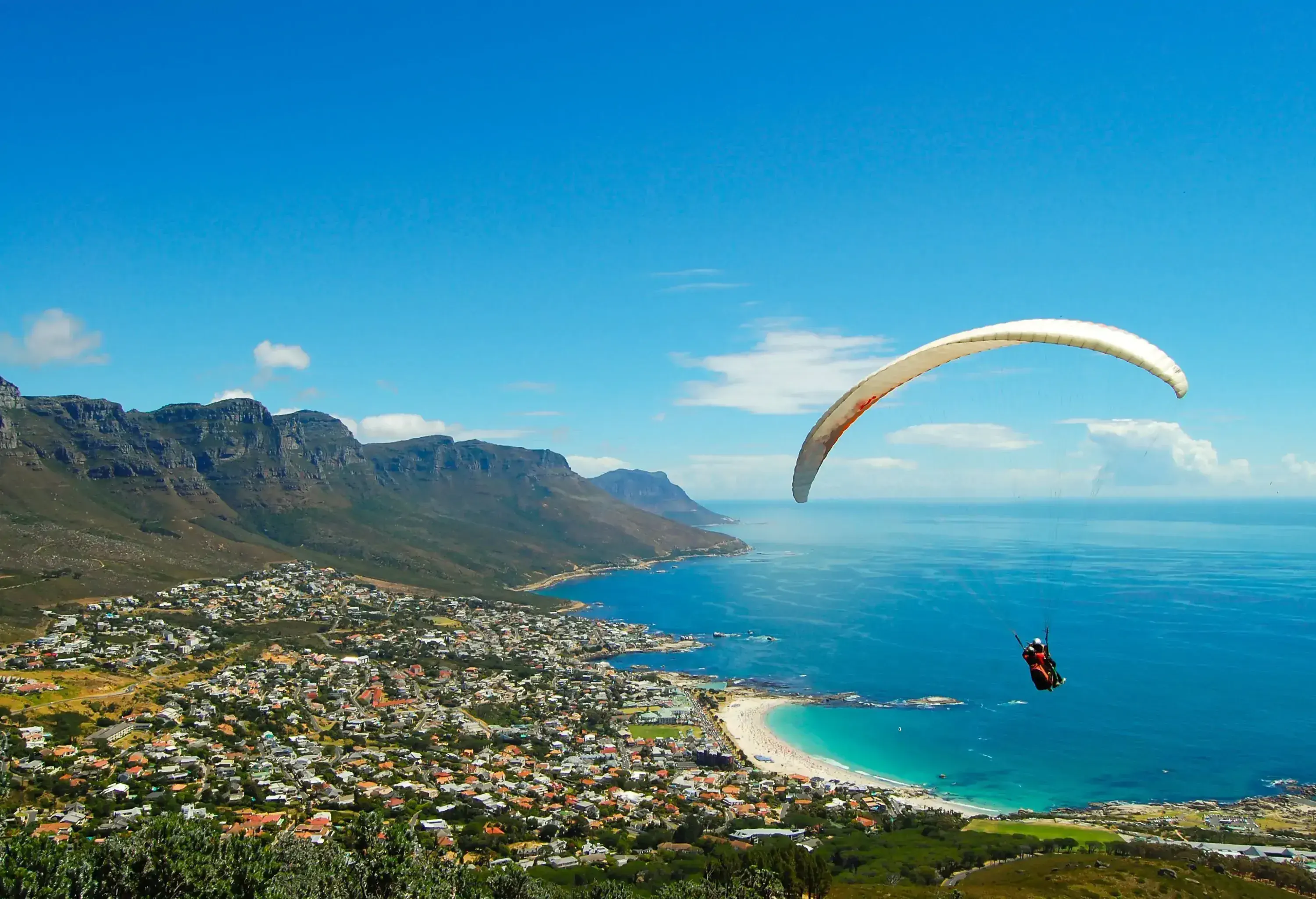 An individual paraglide over the lush coastal city surrounded by the turquoise sea.