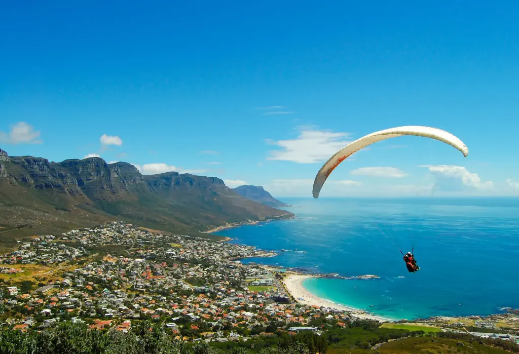 An individual paraglide over the lush coastal city surrounded by the turquoise sea.