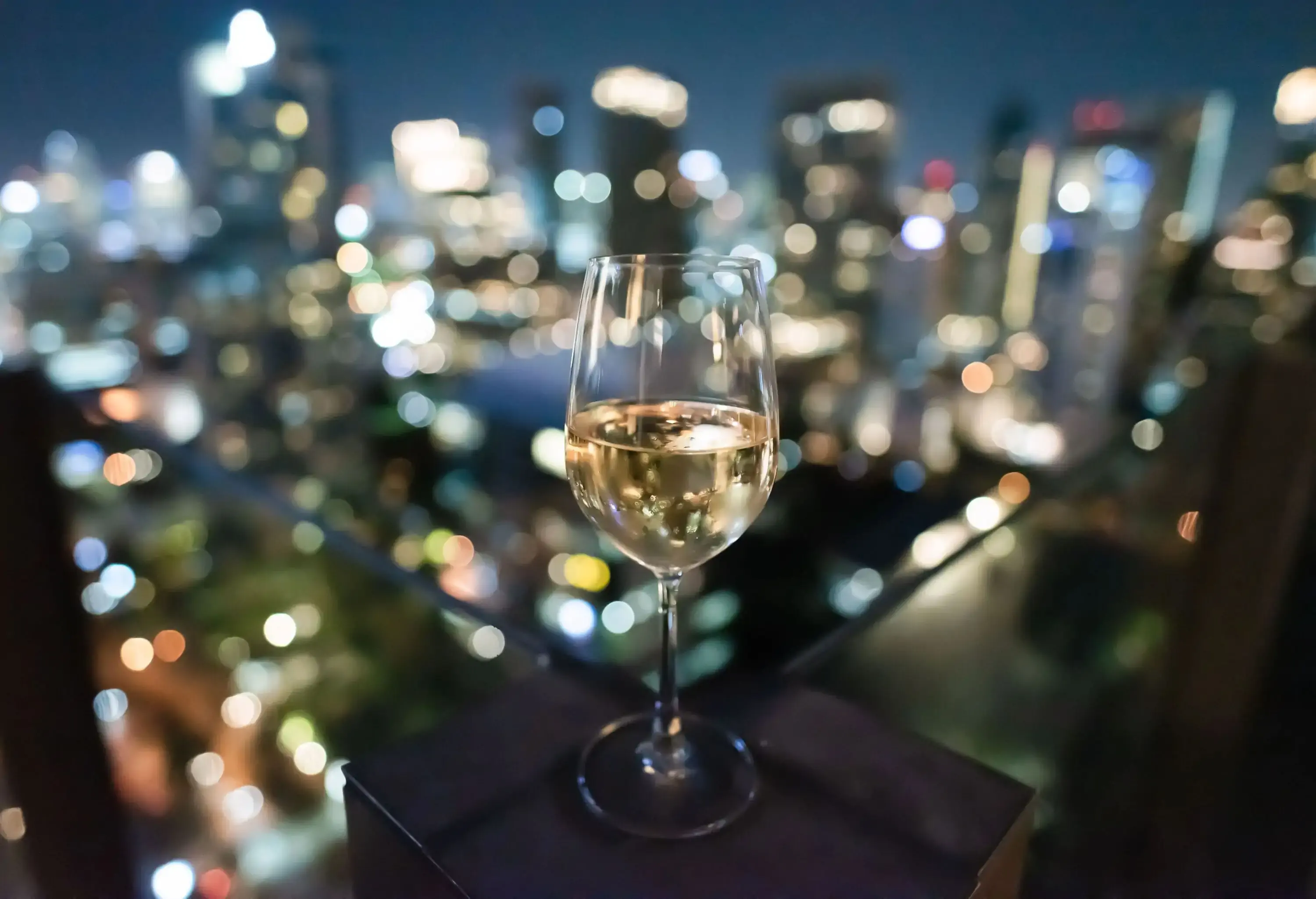 A wine glass set on a fence post with night lights in the background.