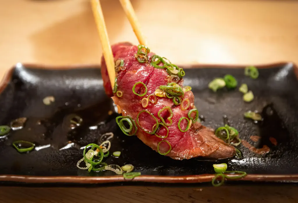 A piece of meat garnished with chopped scallions picked by a chopstick.