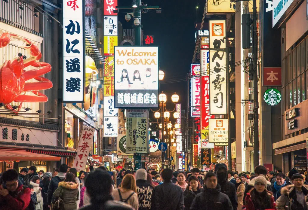 A vibrant night at Dotonbori with dazzling light displays, bustling crowds of people, and an array of eye-catching shop advertisements.