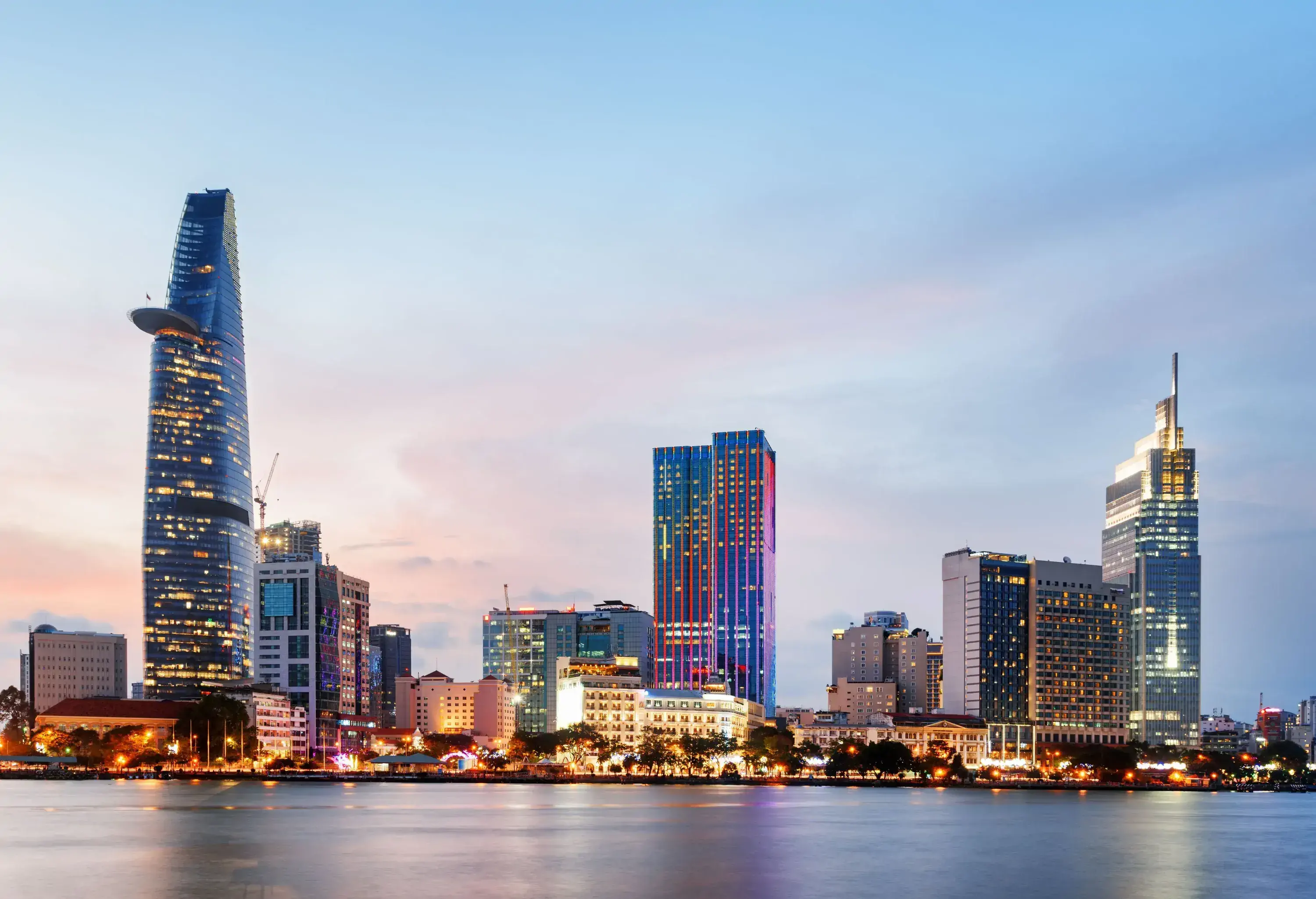 The city skyline illuminated against the clear pinkish-blue sky alongside the broad tranquil river.