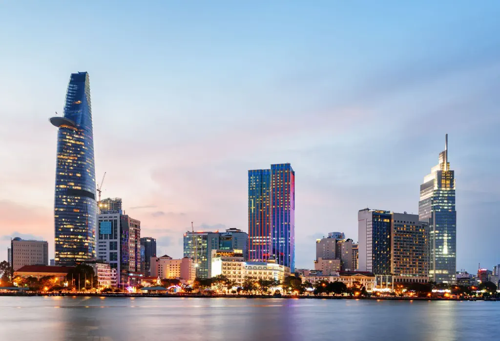 The city skyline illuminated against the clear pinkish-blue sky alongside the broad tranquil river.