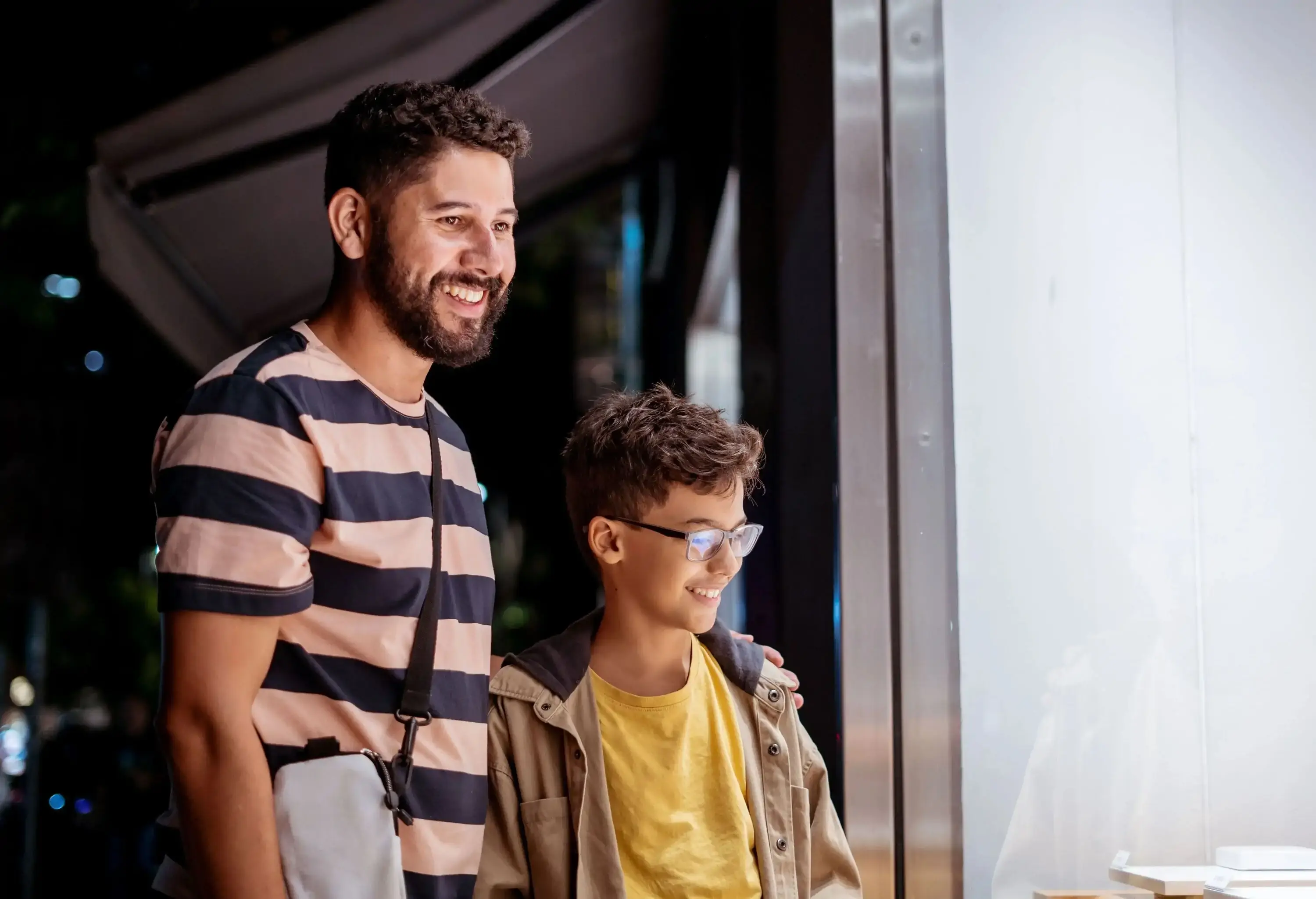 A father and his son stand outside a store with glass window.