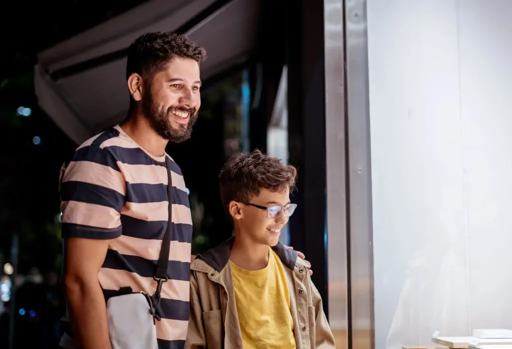 A father and his son stand outside a store with glass window.