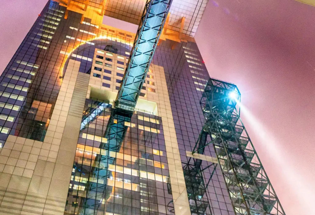 A towering modern building with a glass facade is seen from street level at night.