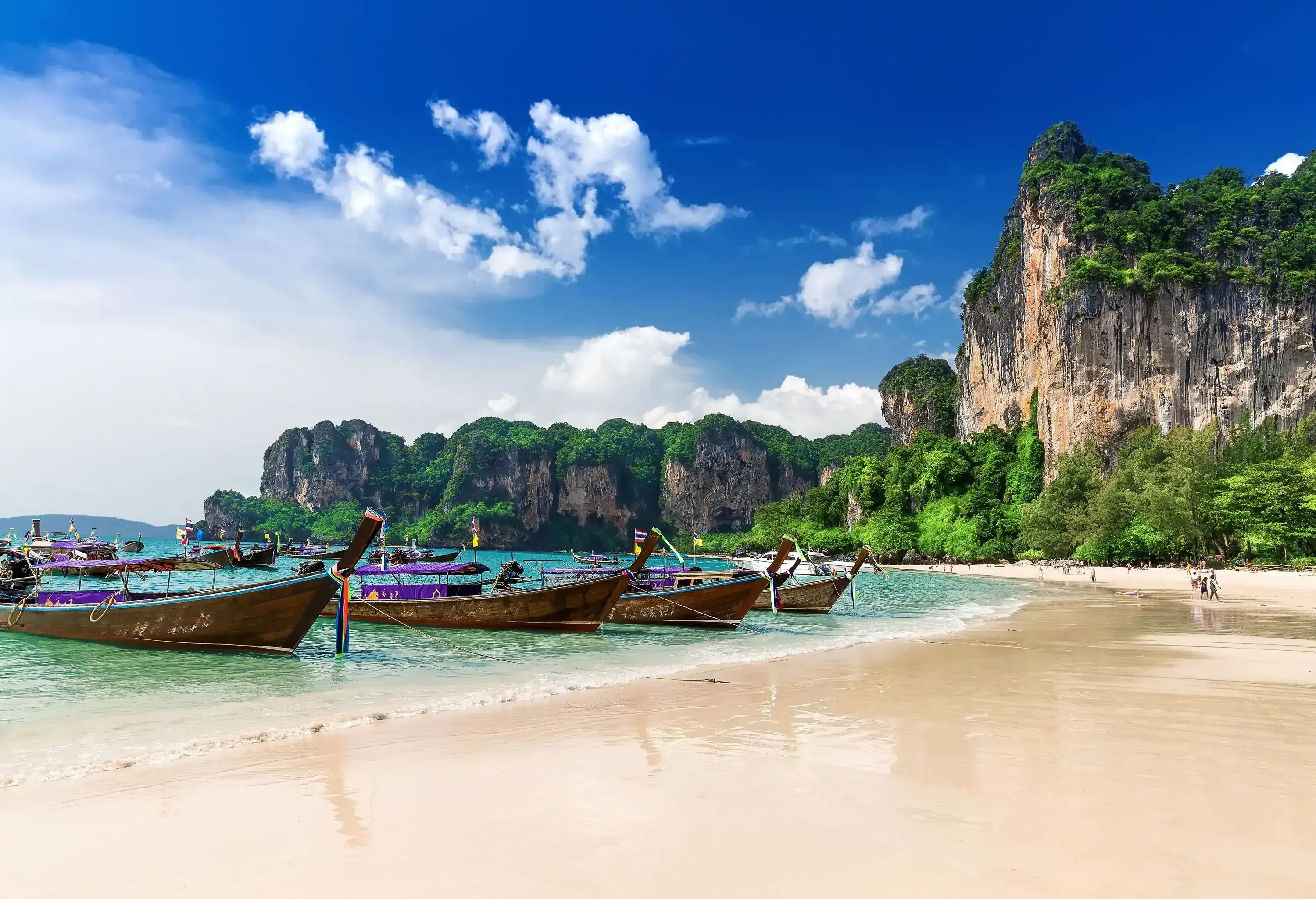 Long-tail boats anchored on a white beach along the verdant dramatic cliffs.