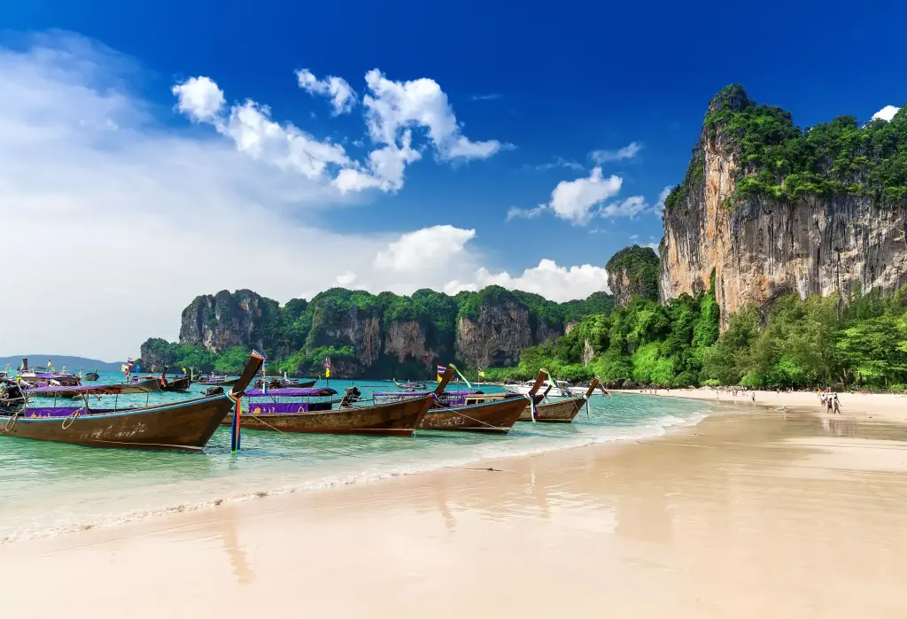 Long-tail boats anchored on a white beach along the verdant dramatic cliffs.