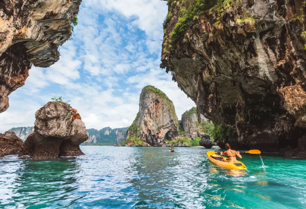 A woman rides a yellow kayak as she paddles along the steep rock cliffs of a beach.