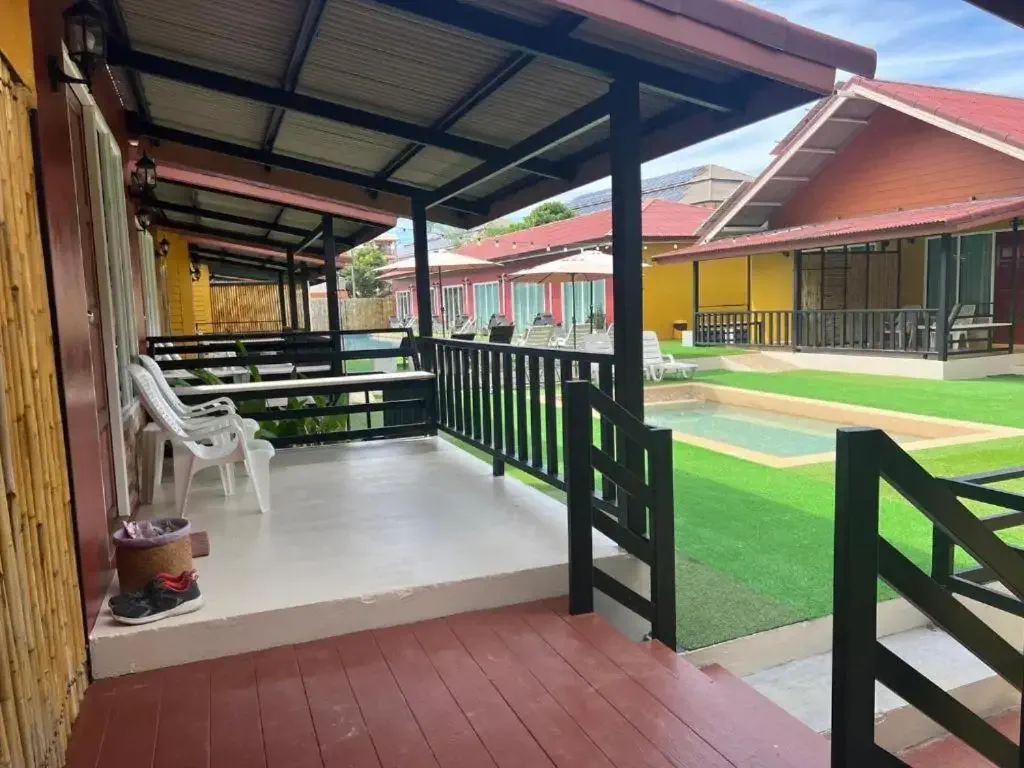 Covered porch with white chairs and a table, overlooking a courtyard with green artificial grass and a small pool. 