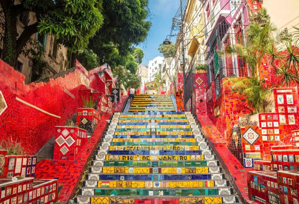 A vibrant and colourful outdoor staircase adorned with mosaic tiles leads to a charming street, beautifully bordered by houses.
